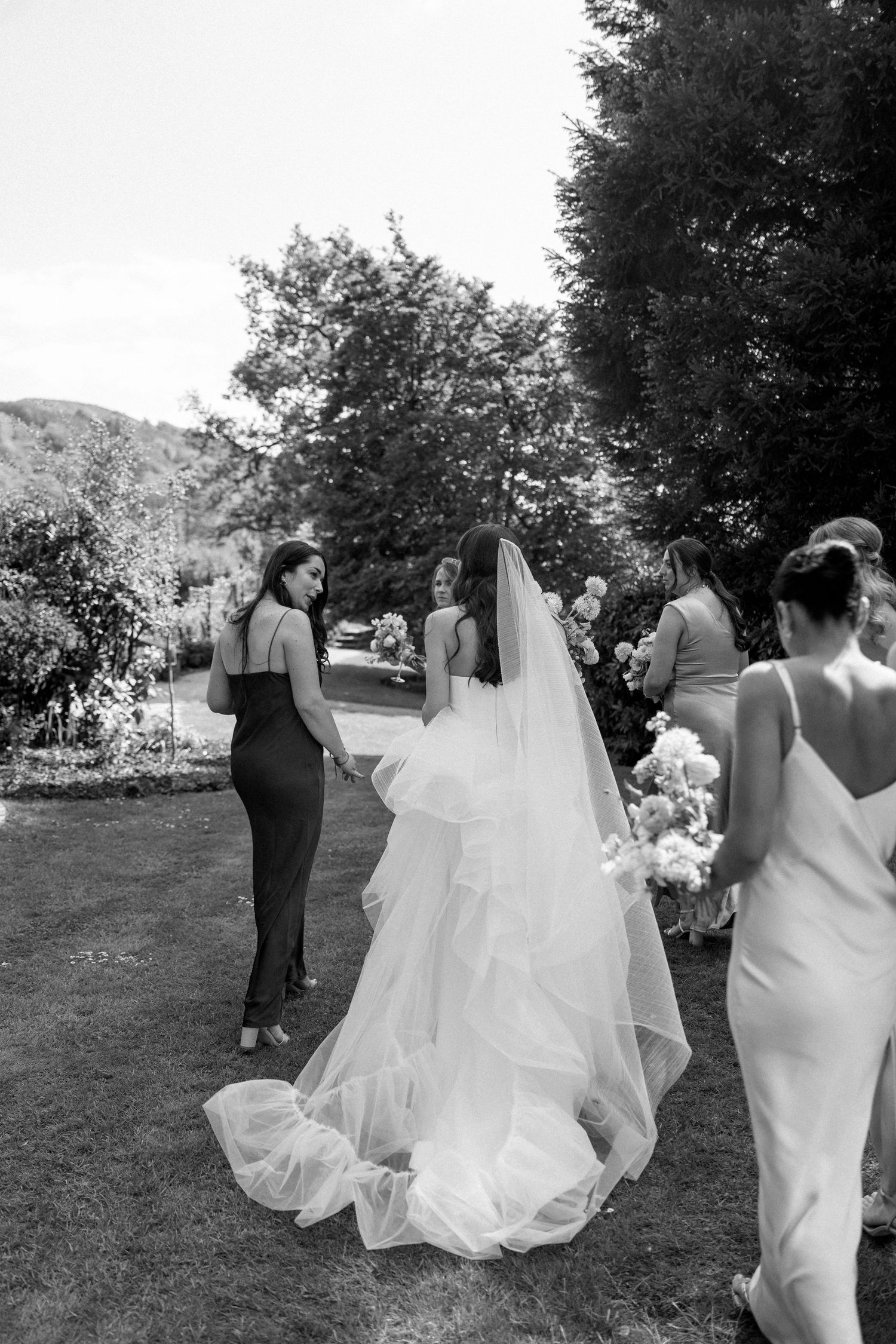 A wedding party walks together across a grassy lawn in black and white.