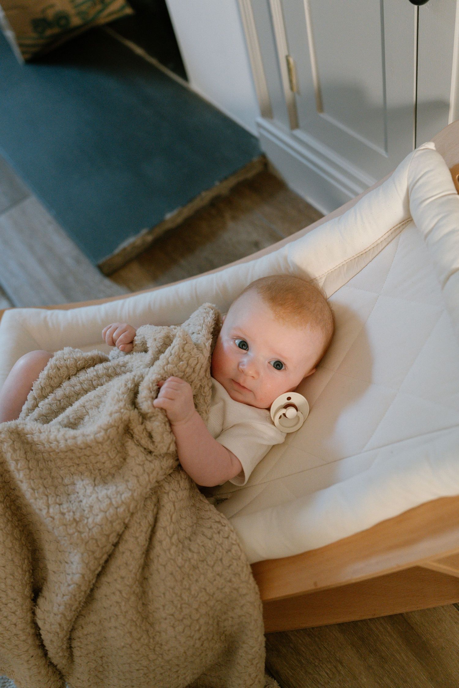 A baby resting peacefully in white bedding with a beige textured blanket.
