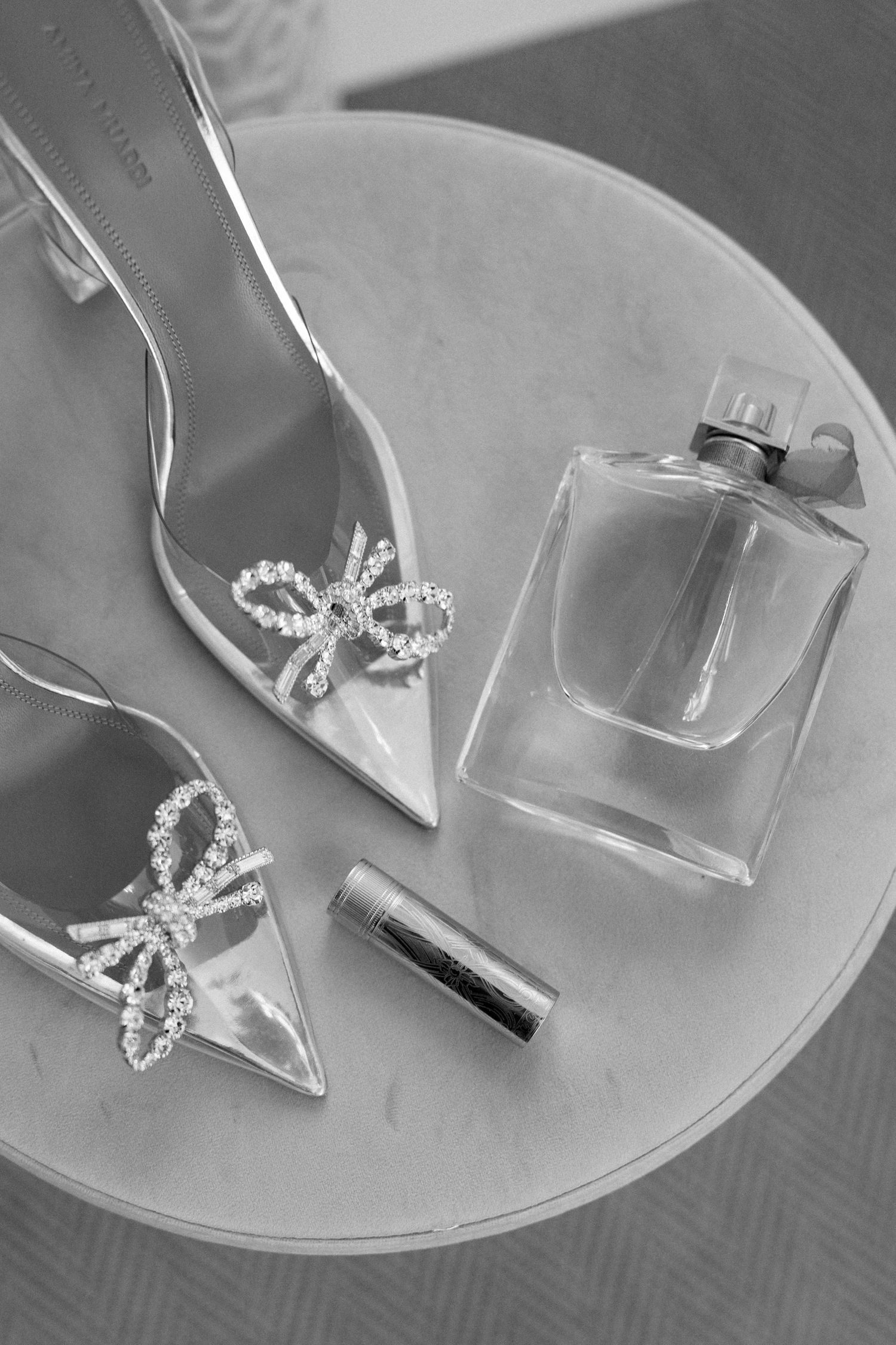Crystal-embellished bridal shoes and perfume bottle arranged on round table.