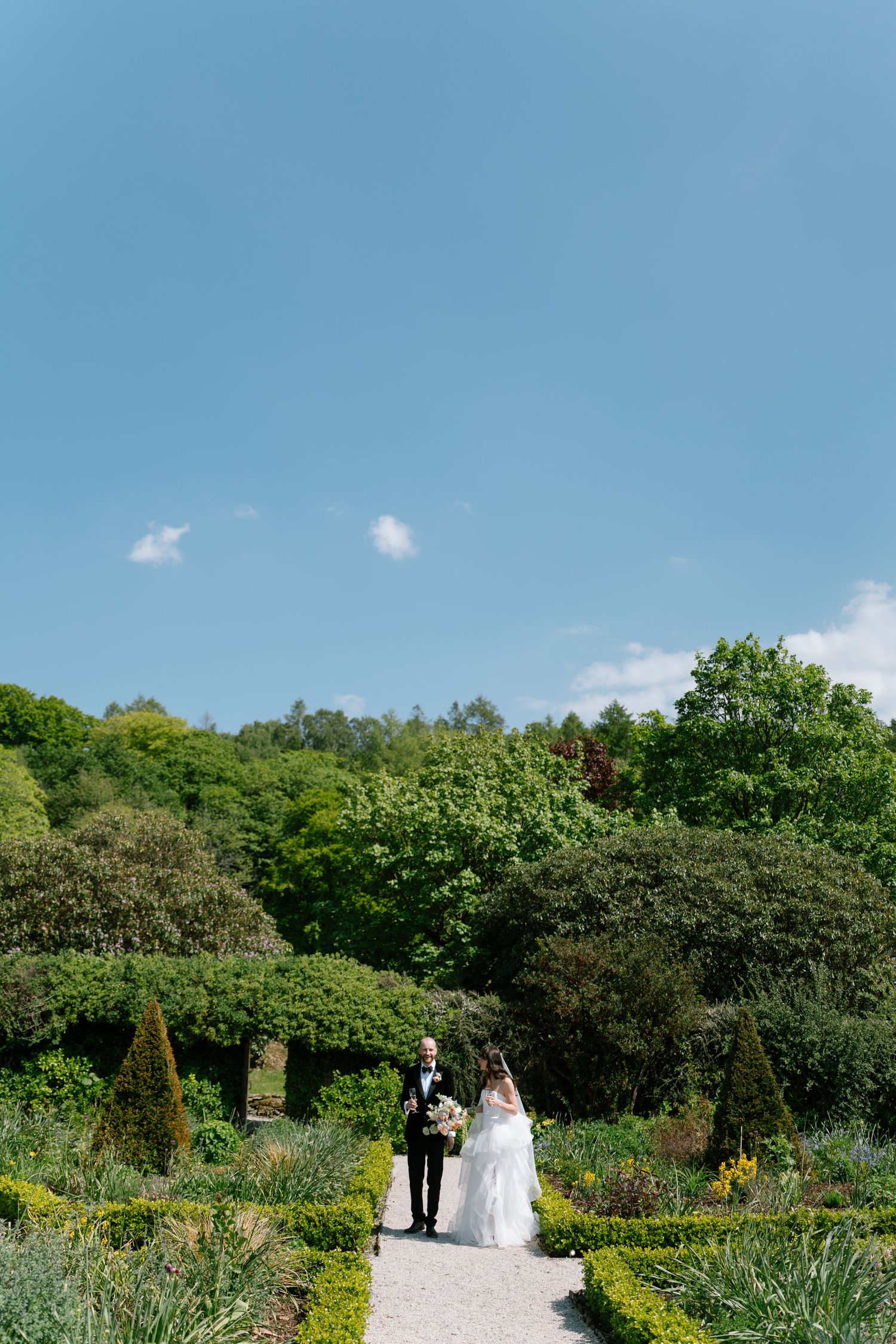 Garden wedding procession under bright blue skies with lush greenery.
