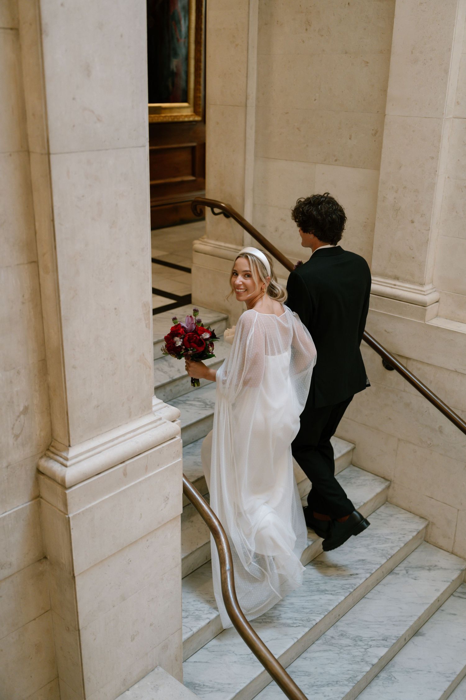 A bride in white and groom in black descending elegant marble stairs in a sequence of photos.