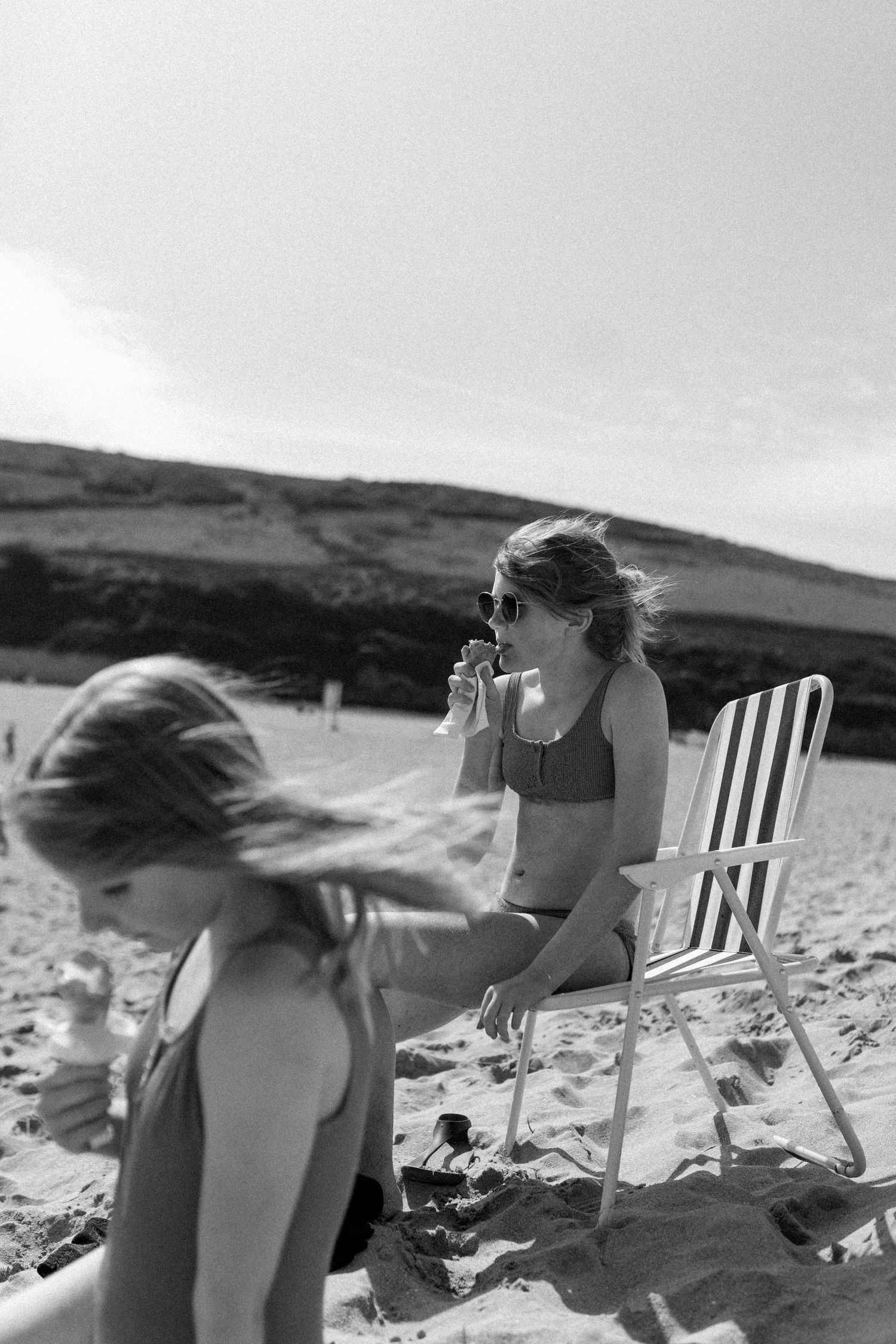 People relaxing in beach chairs along a sandy shoreline on a sunny day.