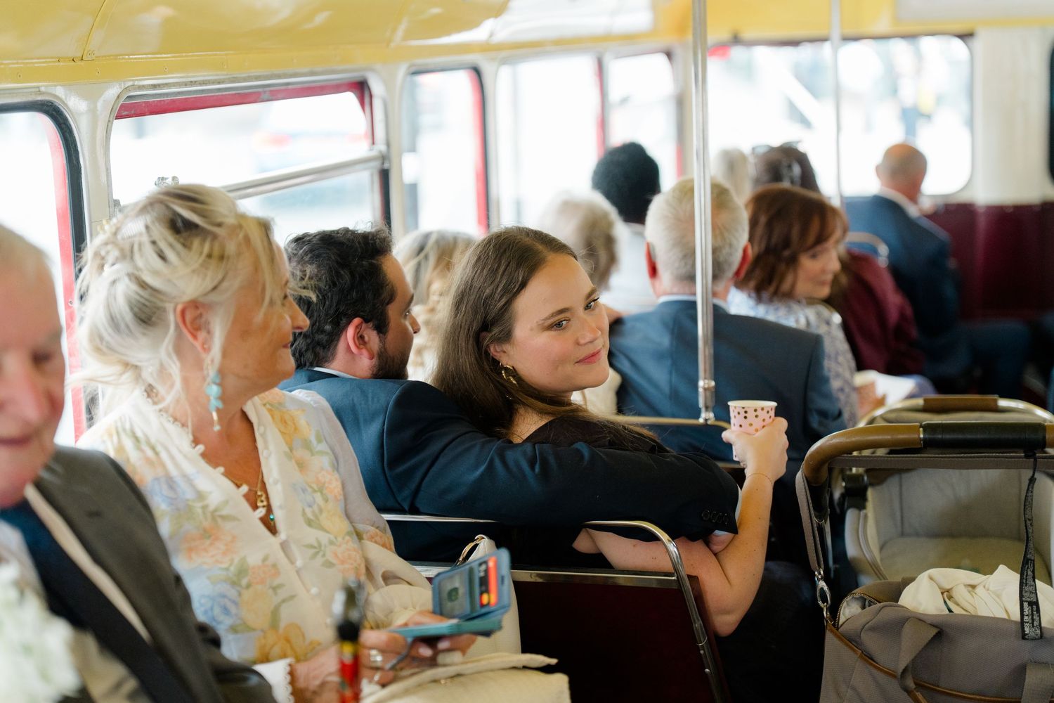 Wedding guests socializing and smiling aboard a vintage red double-decker bus during a special celebration.