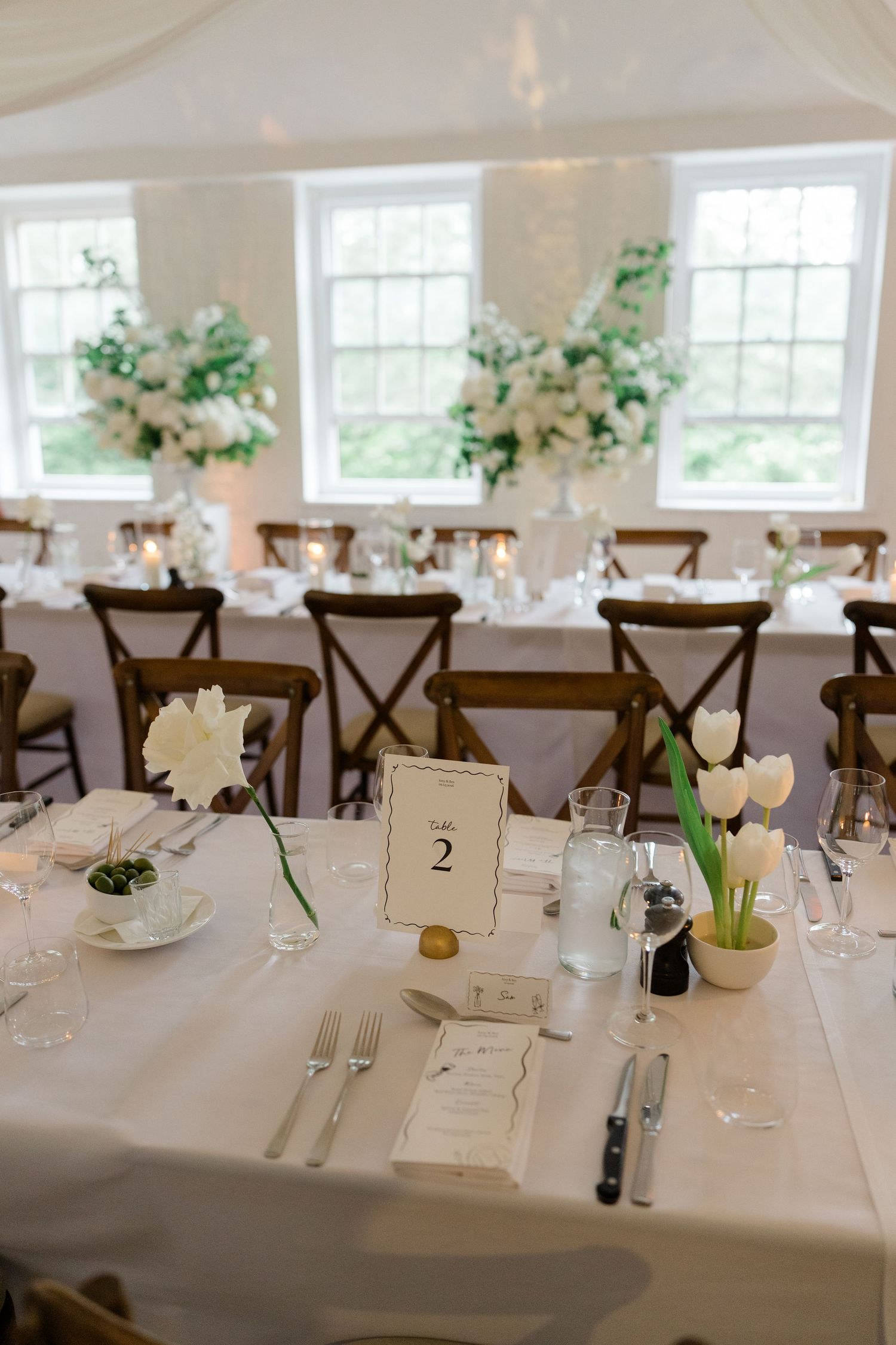 Elegant wedding reception table setting with white tulips, candles, and floral centerpieces.
