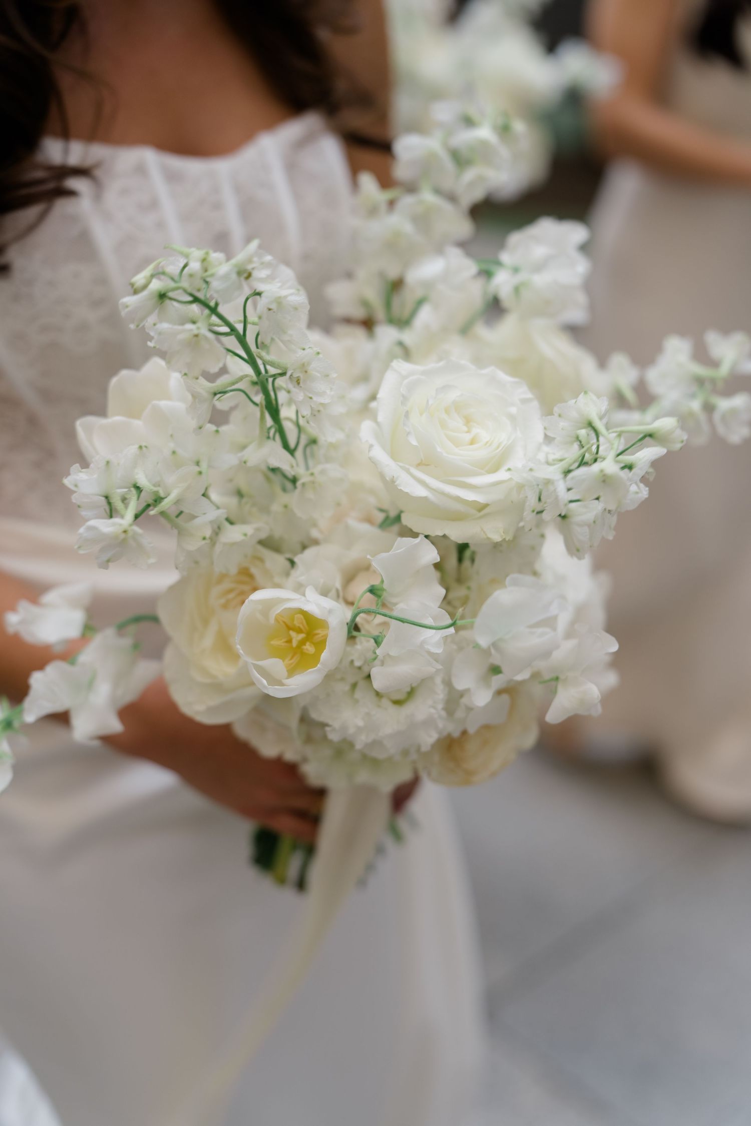 Bride holding a lush white wedding bouquet featuring roses, tulips, and sweet peas.
