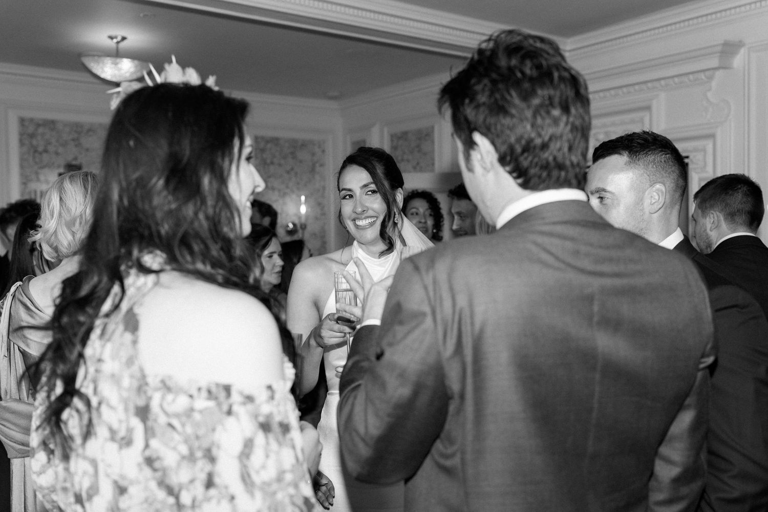 Bride laughs joyfully with wedding guests during black and white candid reception cocktail hour photo.