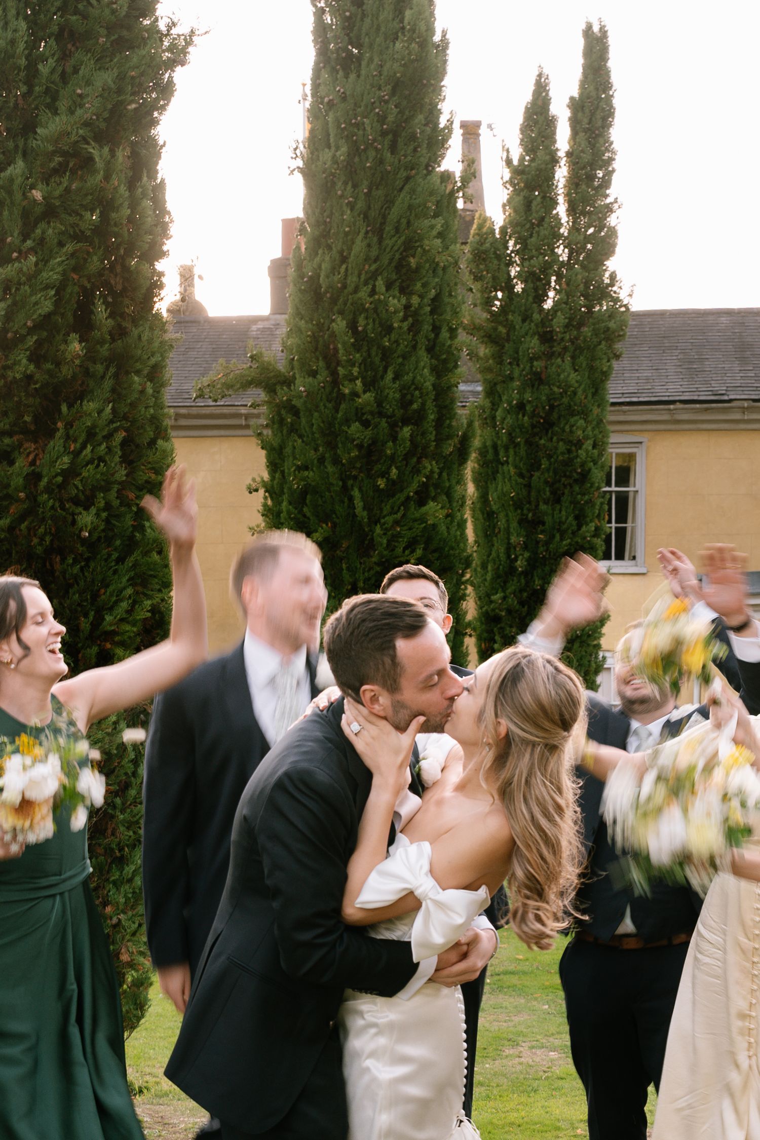 Wedding celebration sequence showing guests toasting and dancing outdoors near cypress trees.