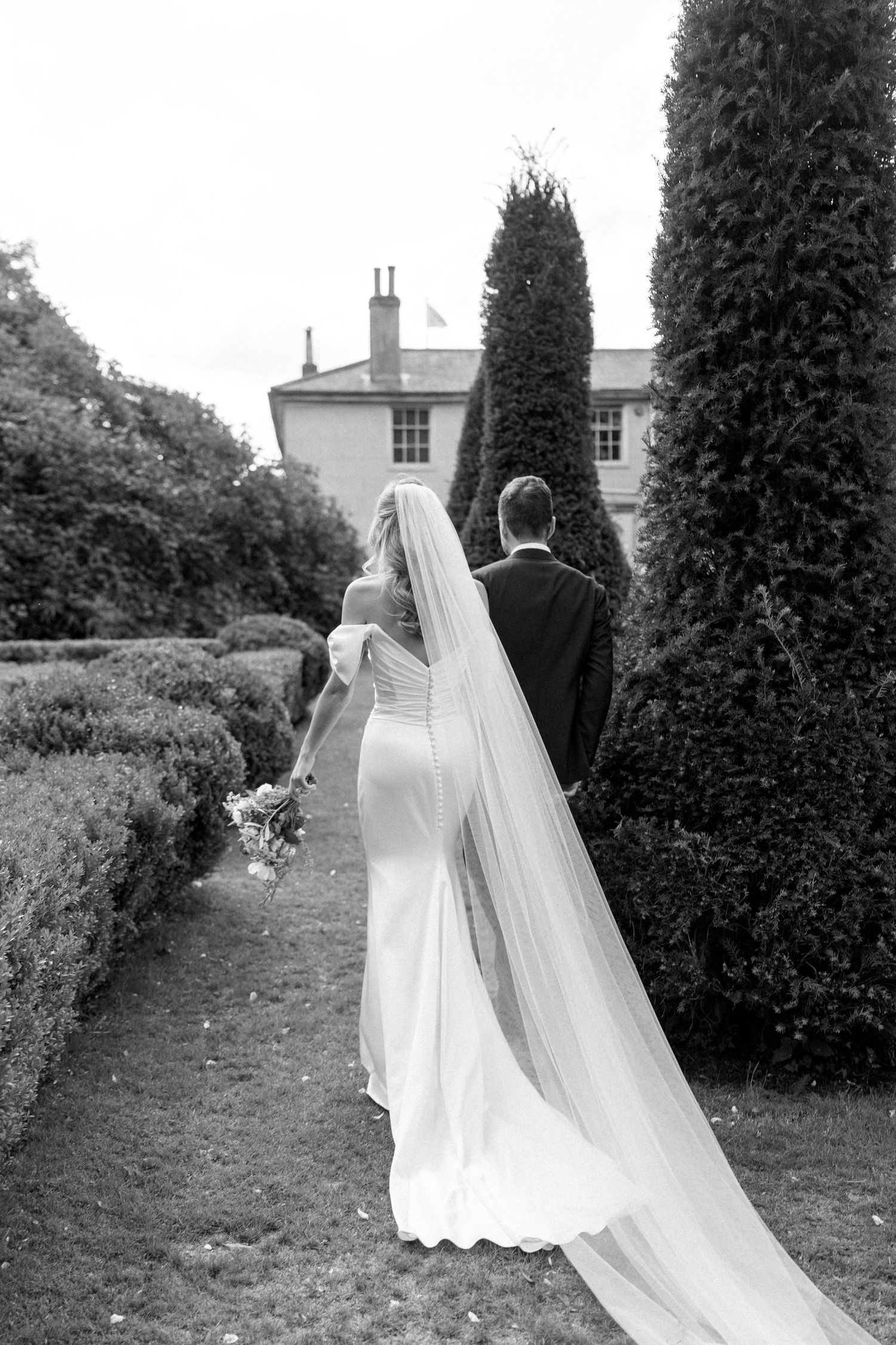 Black and white wedding photography in a formal garden with architectural elements.
