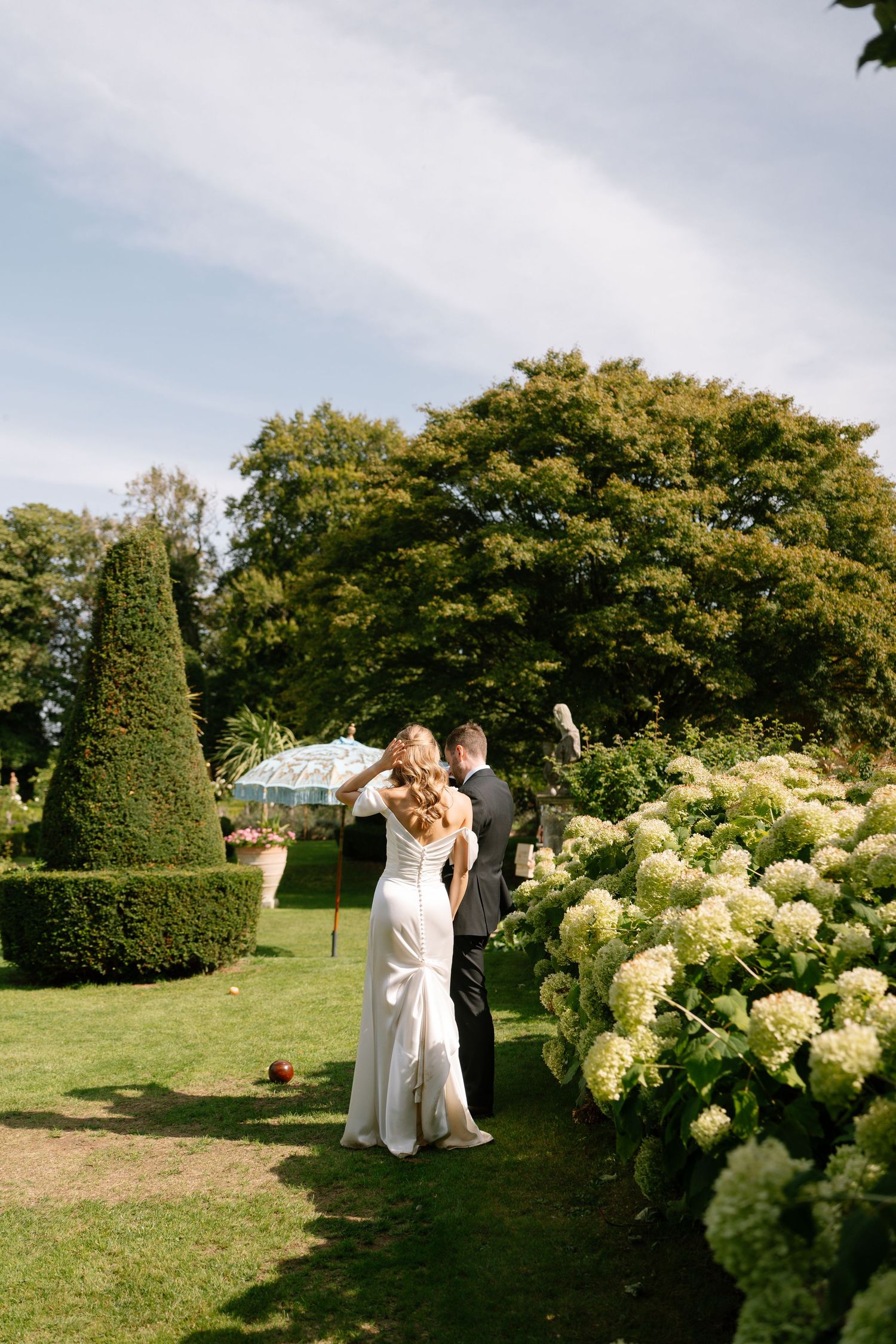Newlyweds share romantic moments among blooming hydrangea bushes in a manicured garden.