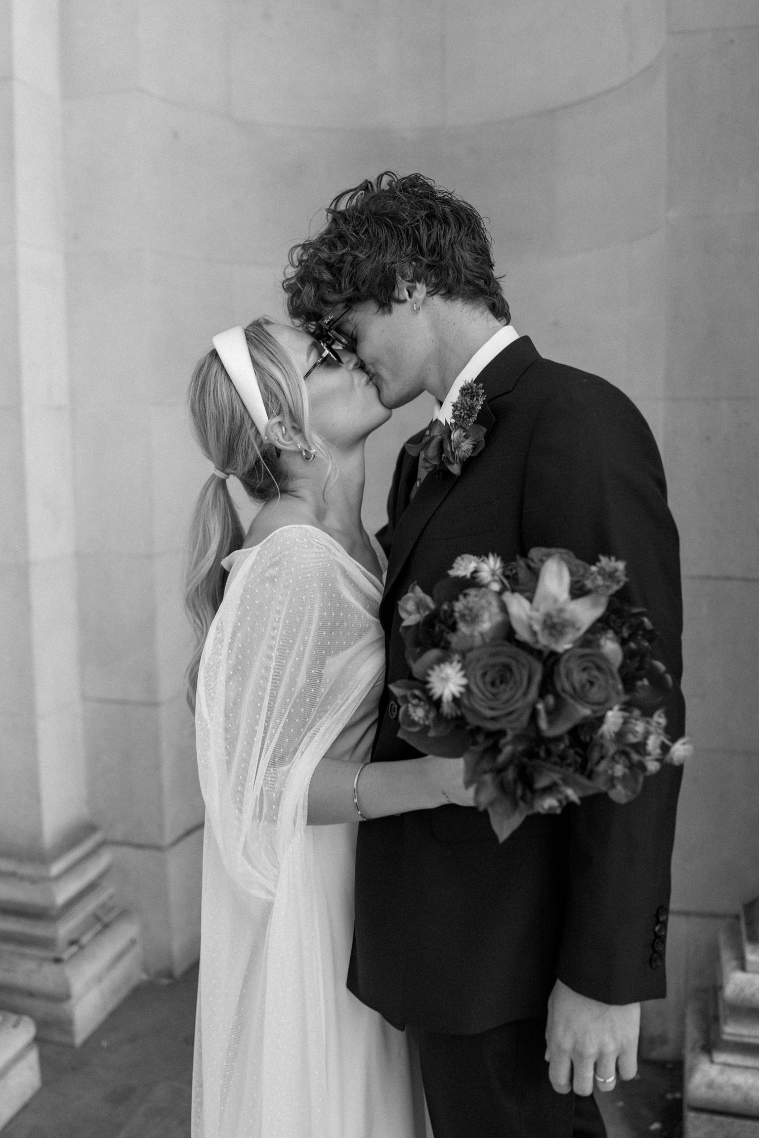 Couple in wedding attire sharing a romantic moment with bouquet of flowers.