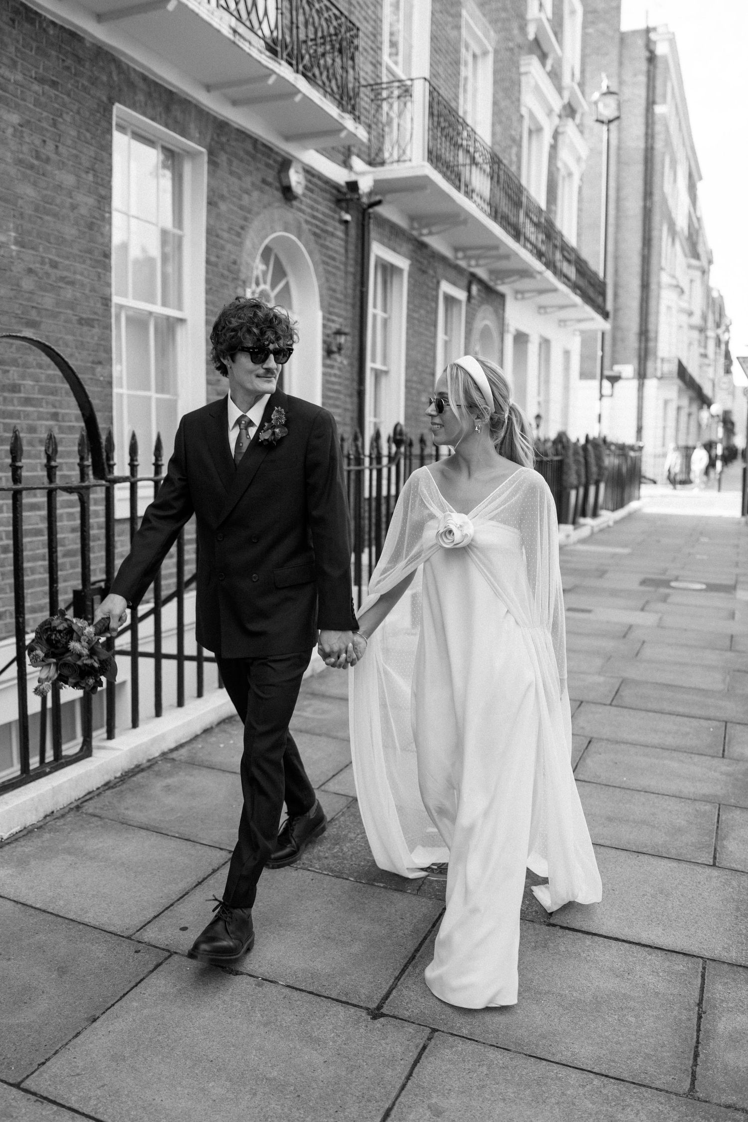 Wedding couple in black and white strolling along a classic London street with iron railings.