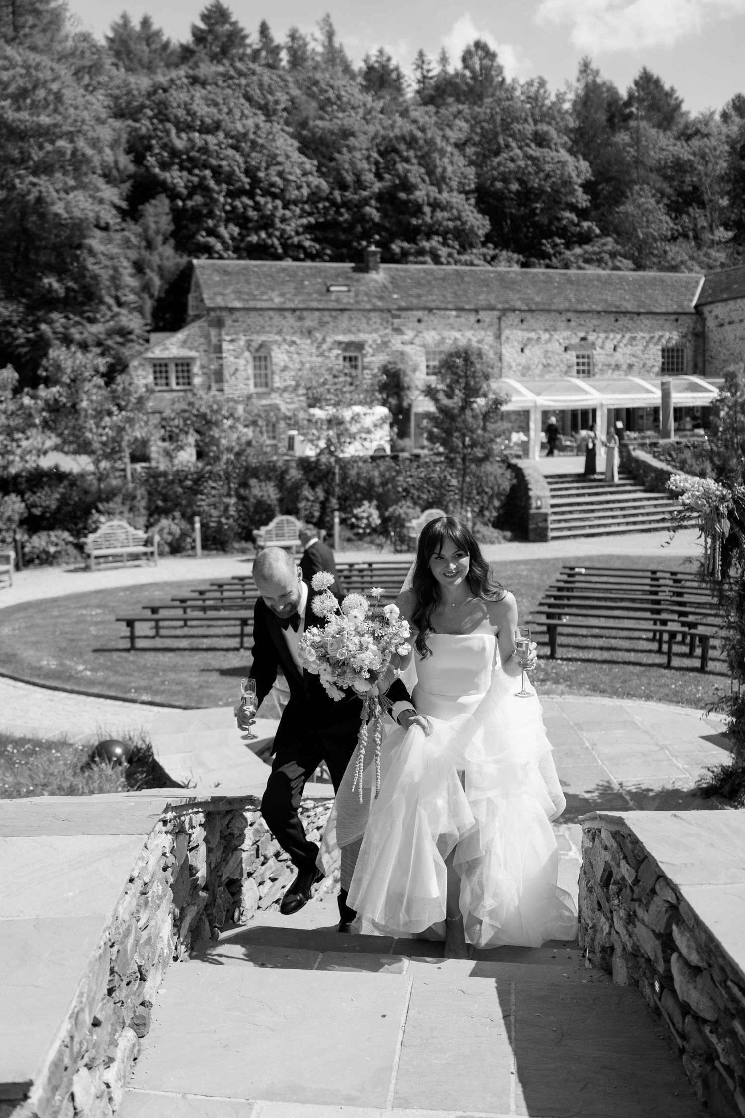 Wedding party walking along a stone path in a garden setting on a sunny day.
