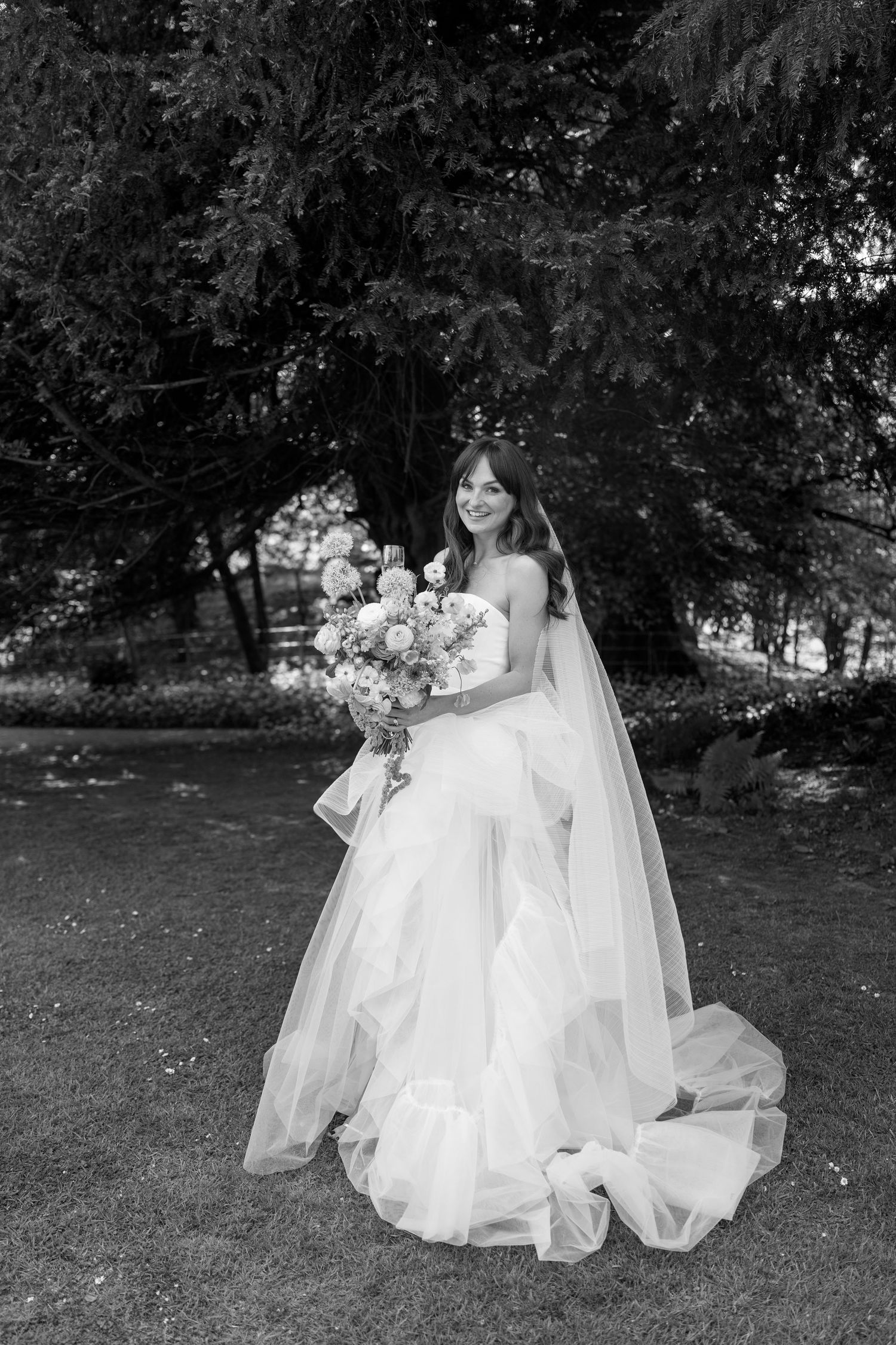 Artistic black and white capture of wedding dresses billowing in outdoor garden.