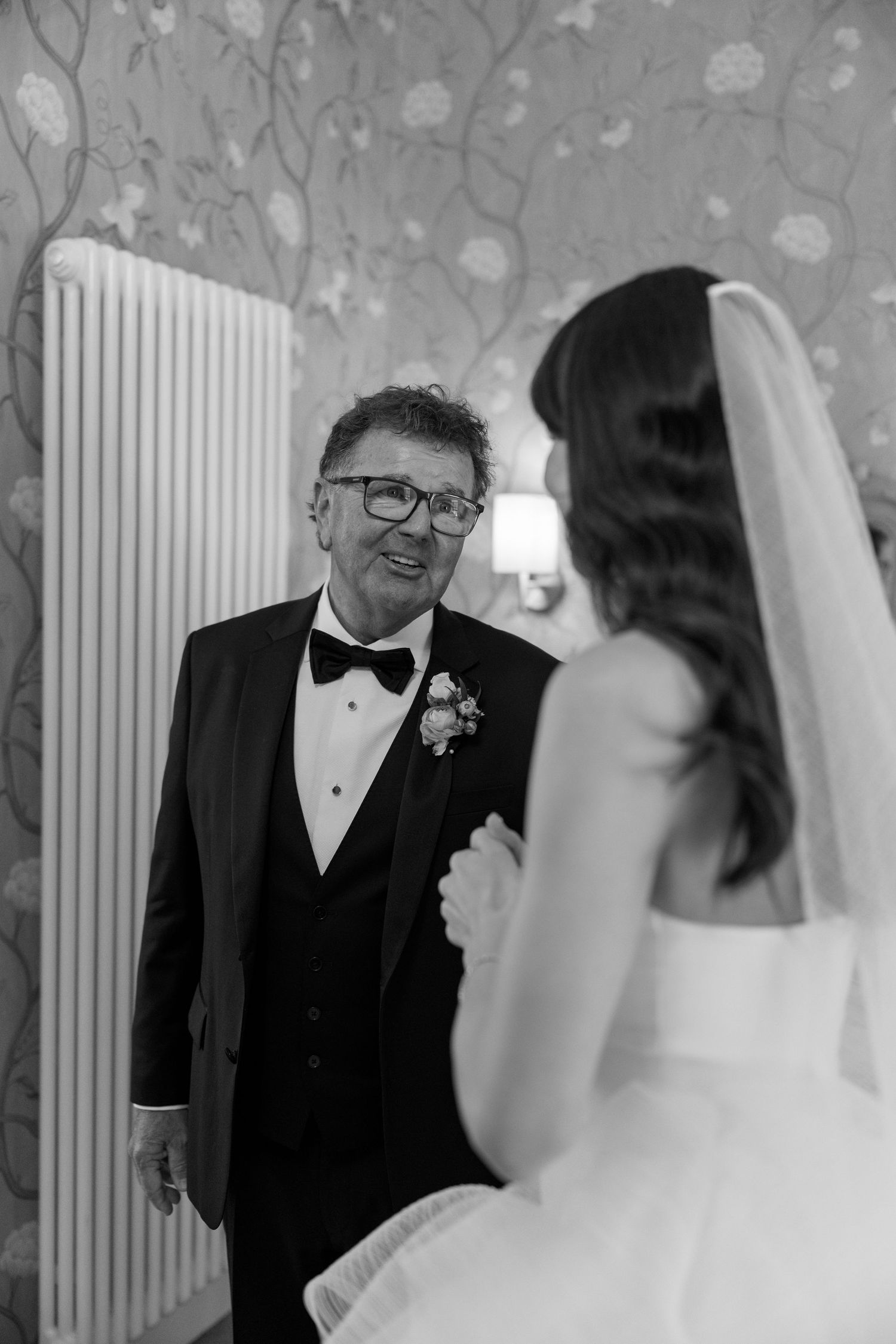 An intimate wedding moment captured in black and white with floral wallpaper backdrop.