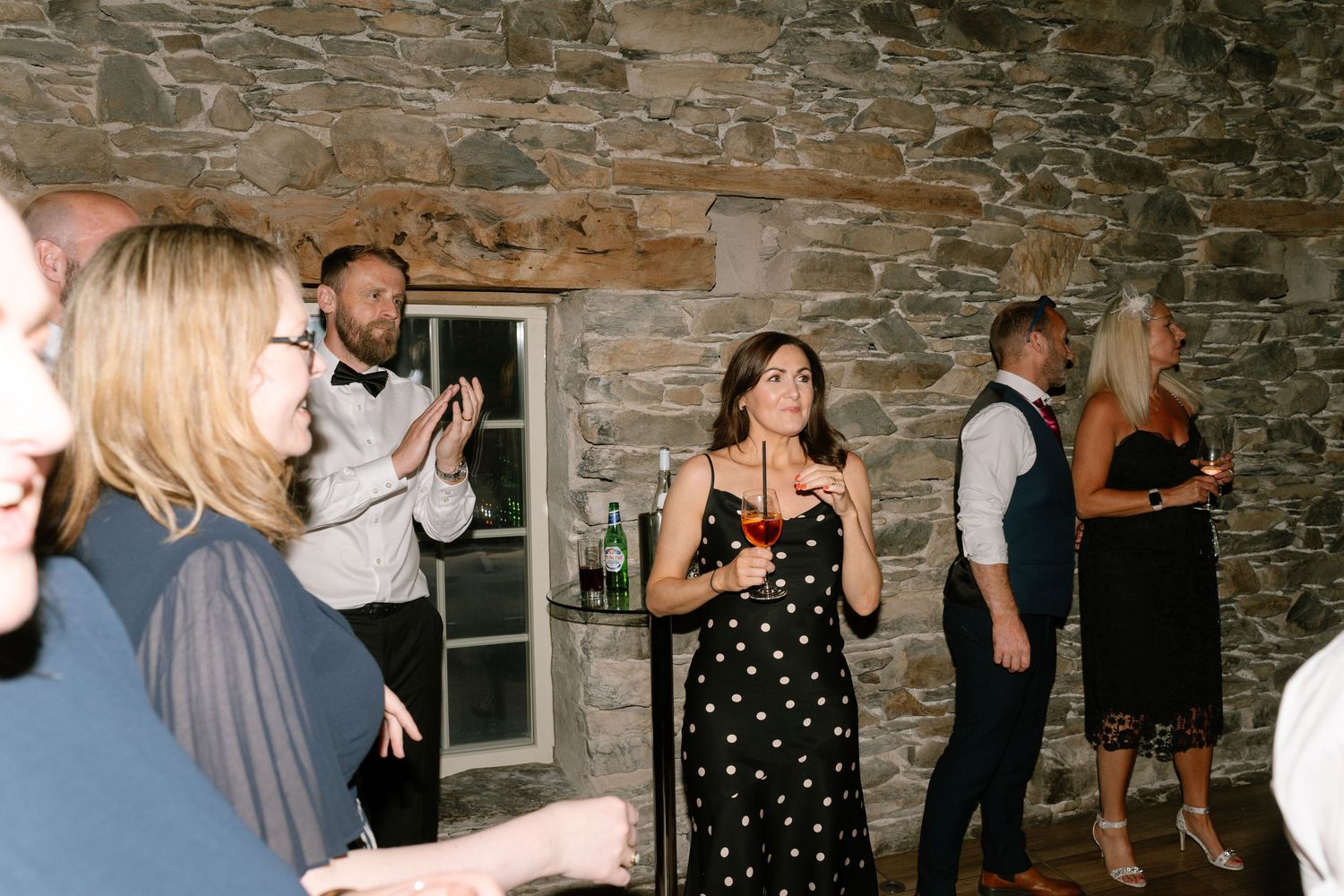 Party guests dancing and socializing in a rustic venue with stone walls and ambient lighting.