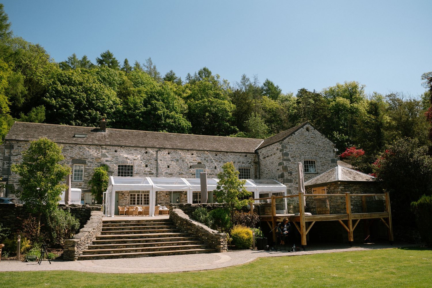 Historic stone building with grand steps and covered patio area surrounded by lush greenery.