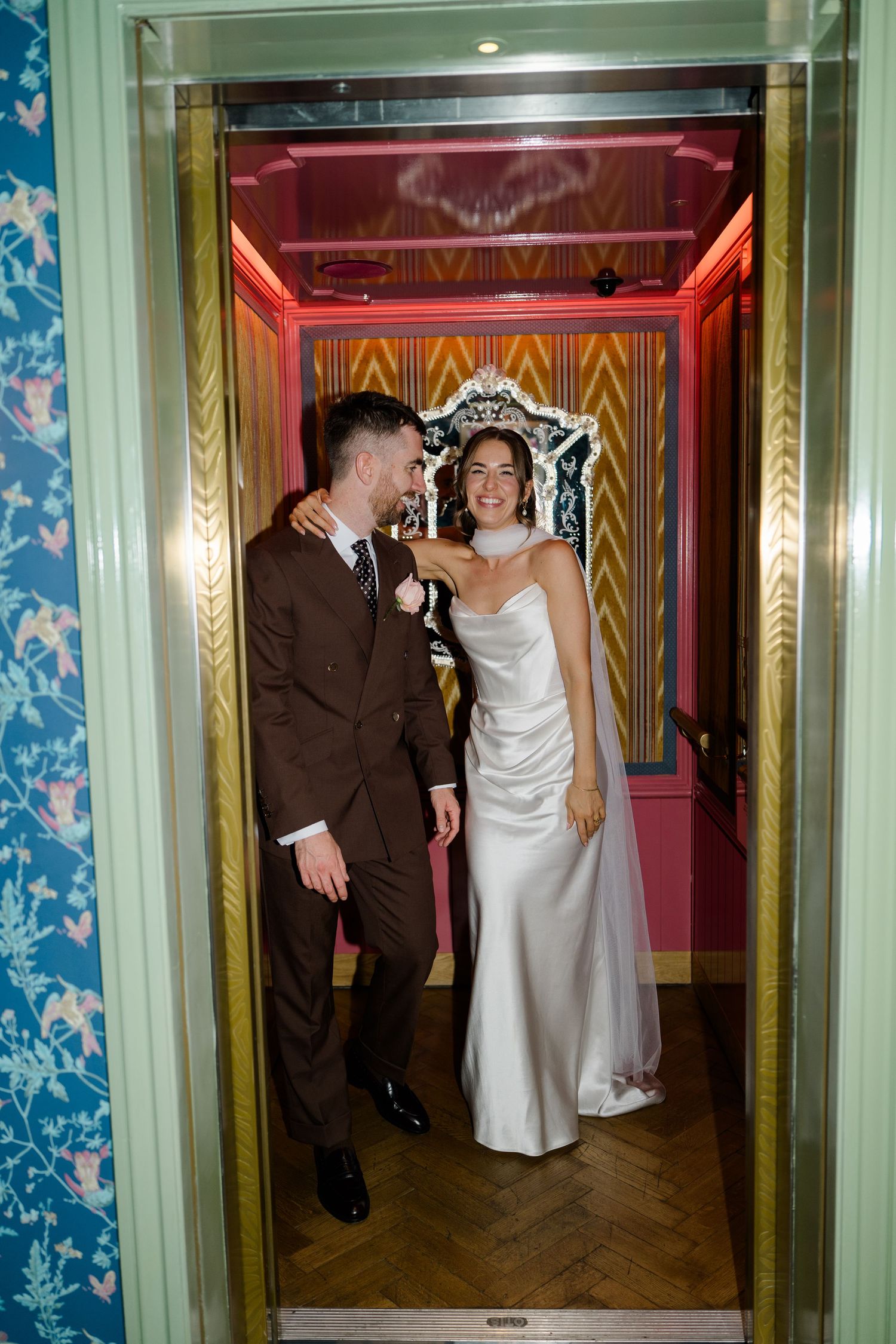 Laughing bride and groom stand together in a colorfully decorated elevator doorway.