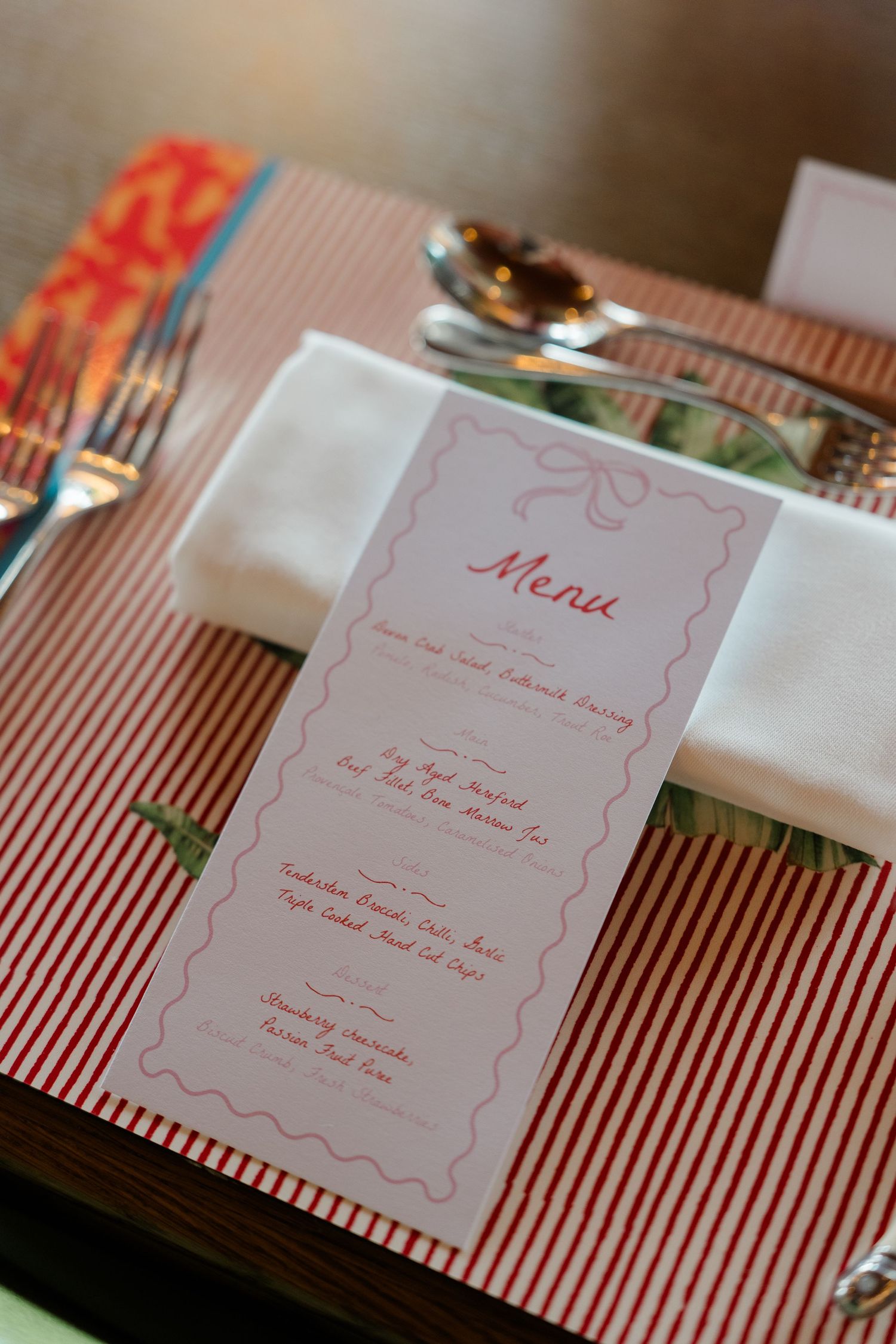 Elegant wedding reception menu card on red striped placemat with silverware and white napkin.