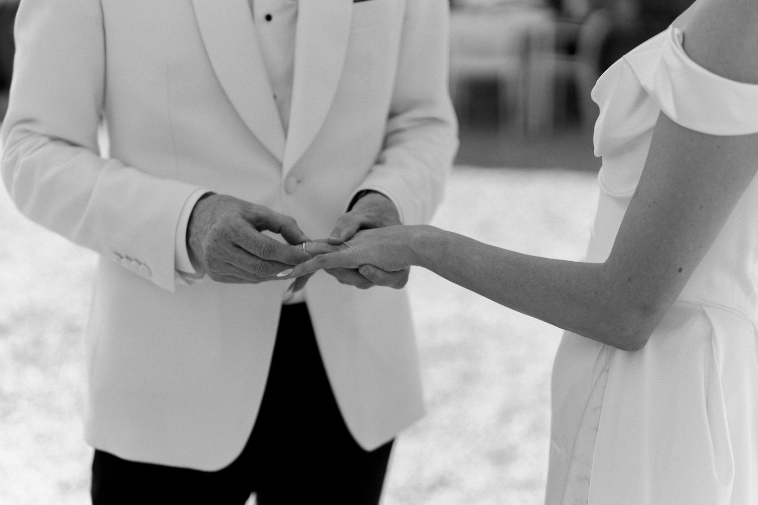 Black and white close-up of groom placing wedding ring on brides hand during ceremony.