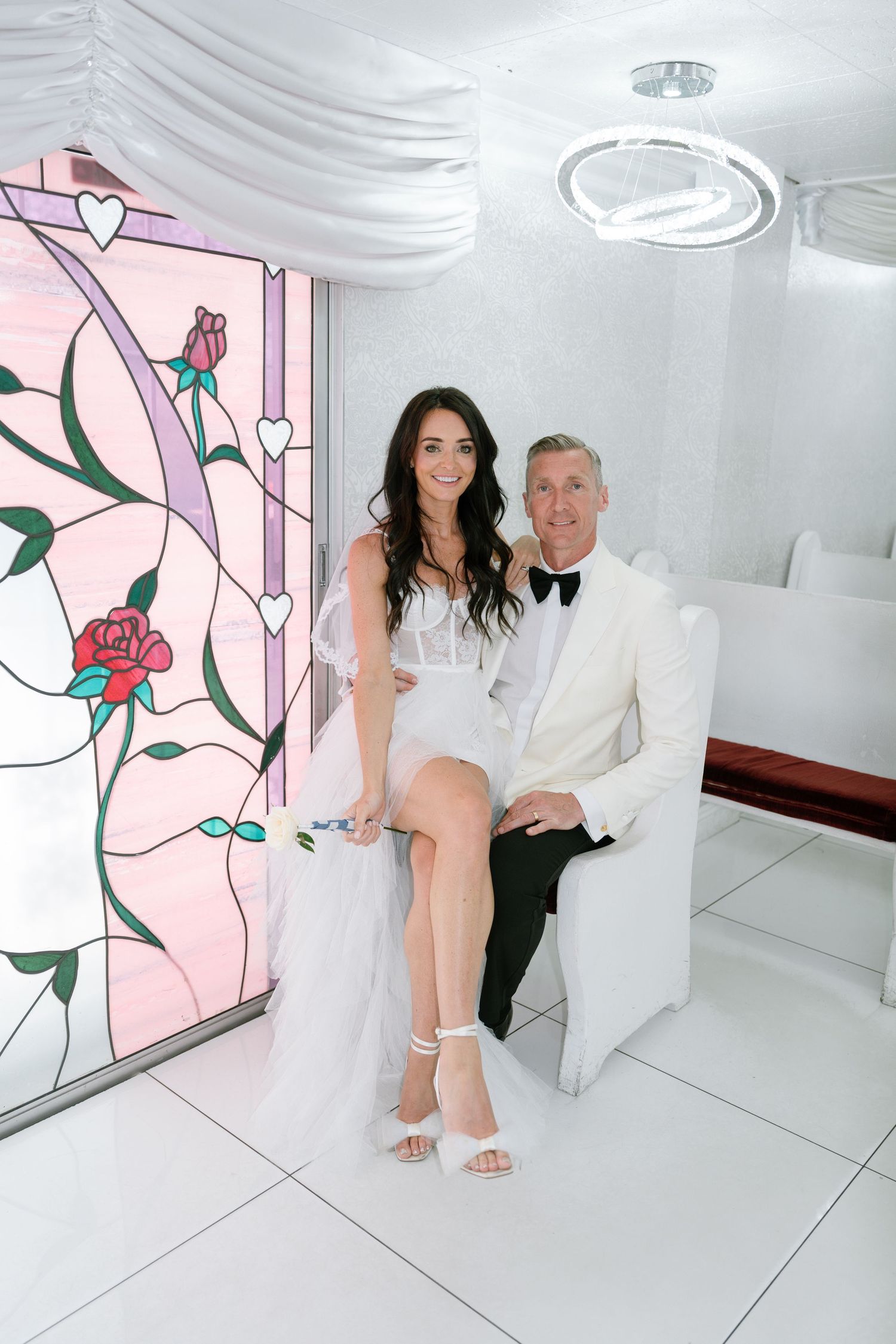Wedding couple sits together in modern white room with pink floral wall art.
