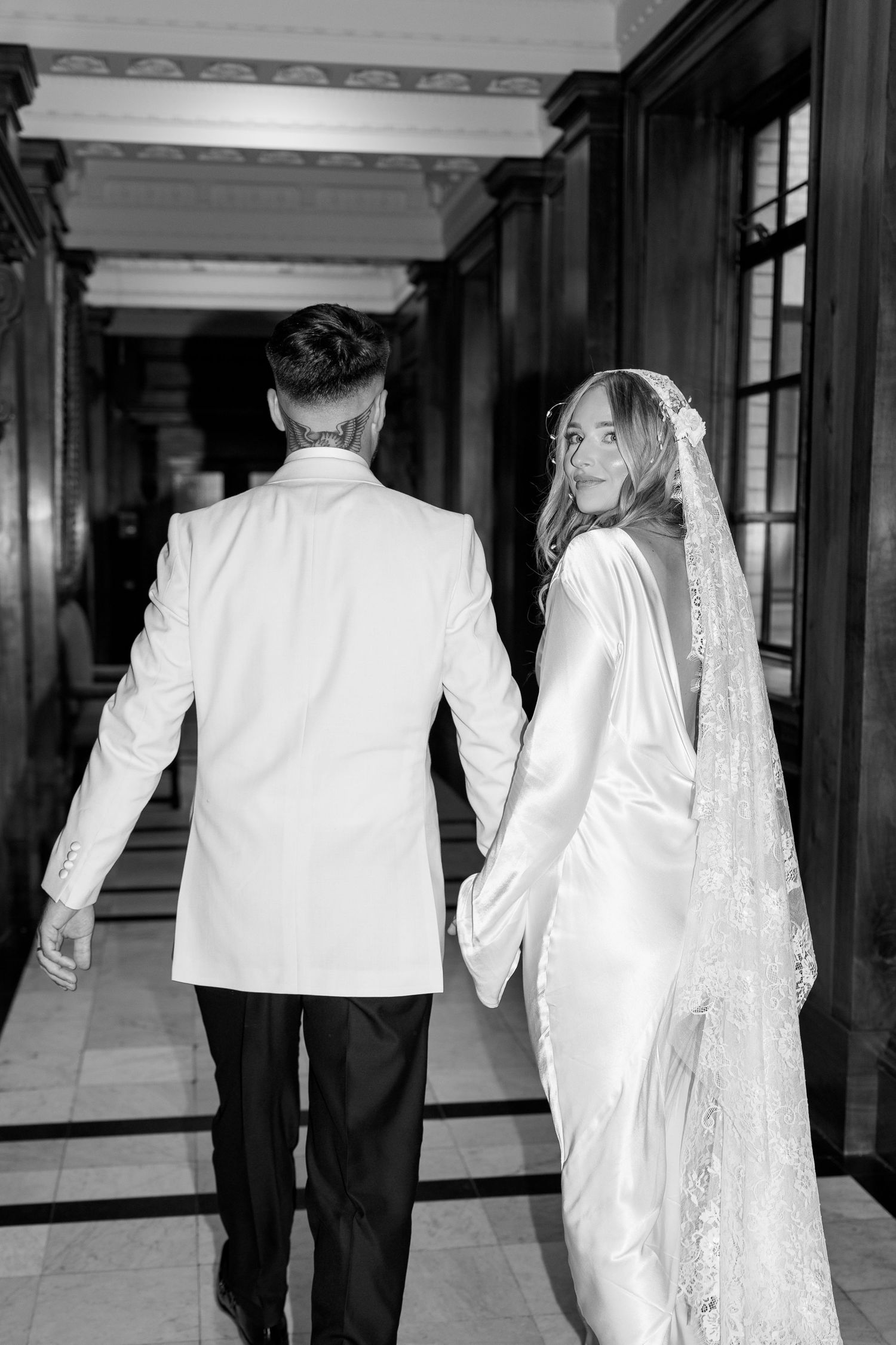 Black and white photo of couple walking down elegant hallway.