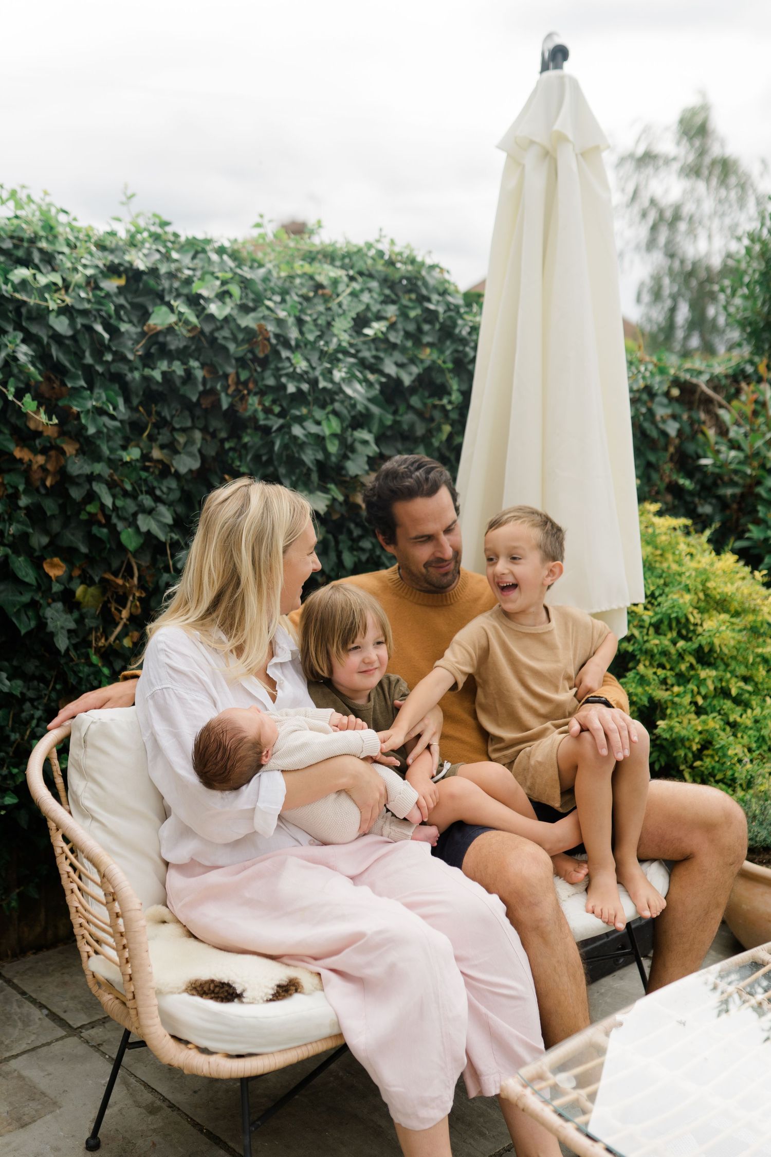 A joyful family gathering on a patio chair under a garden umbrella surrounded by lush greenery.
