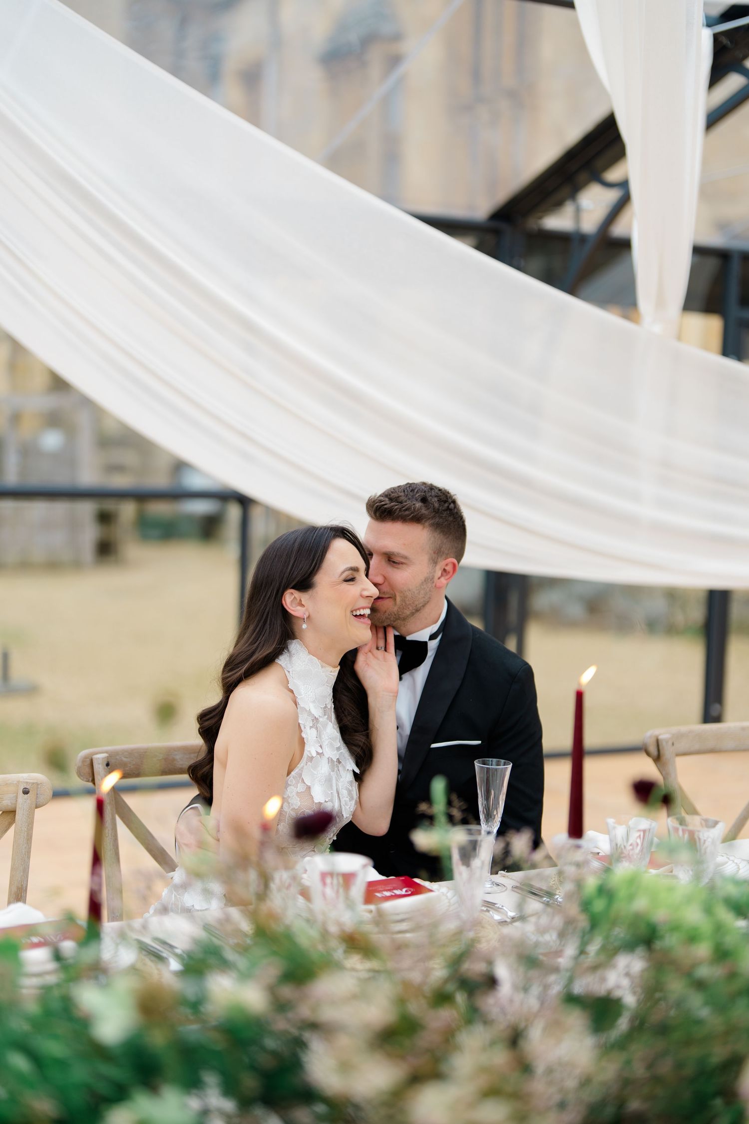 A romantic moment at an elegant wedding reception with white draping decor and floral centerpieces.