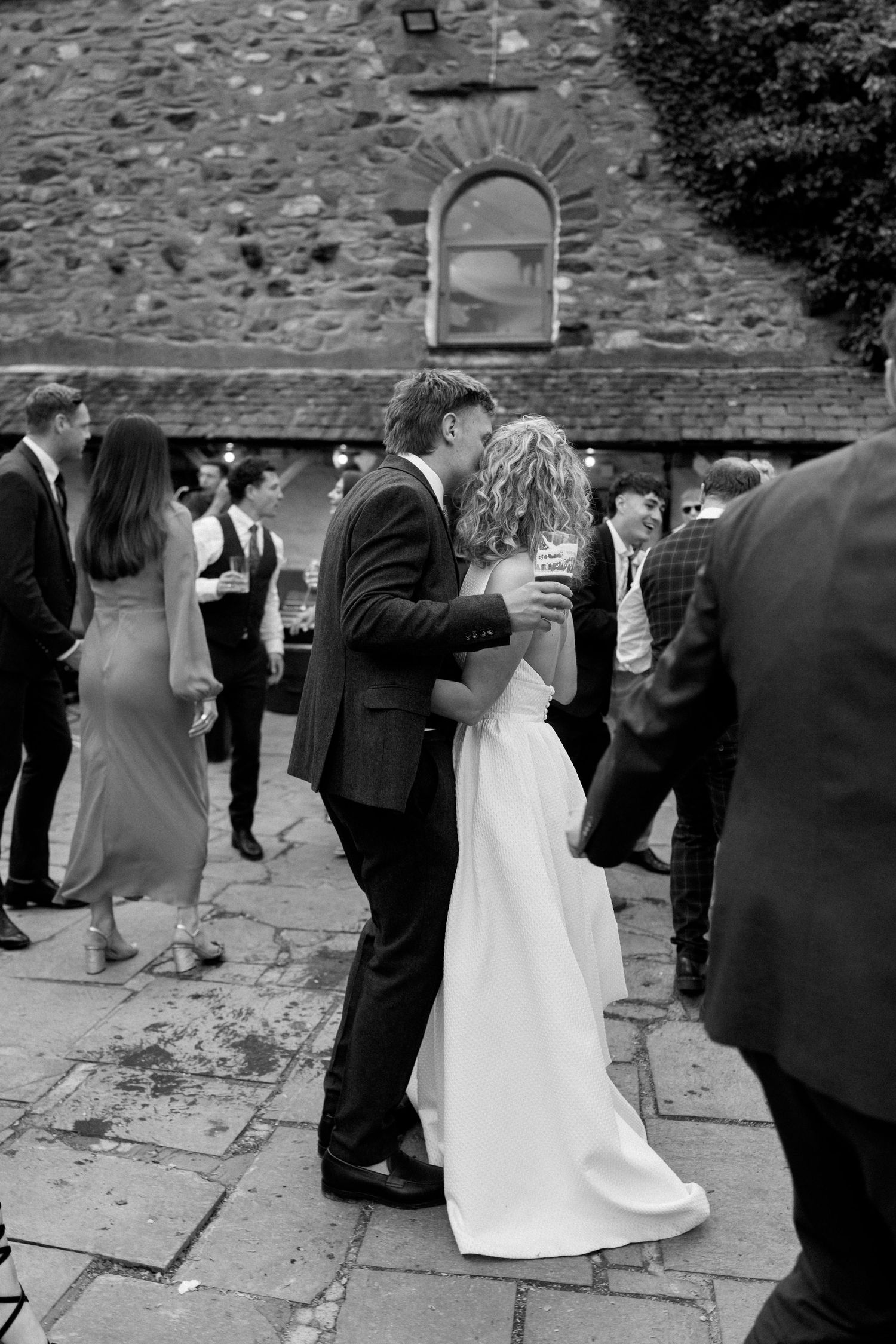 Wedding guests gather around stone courtyard during outdoor celebration in black and white.