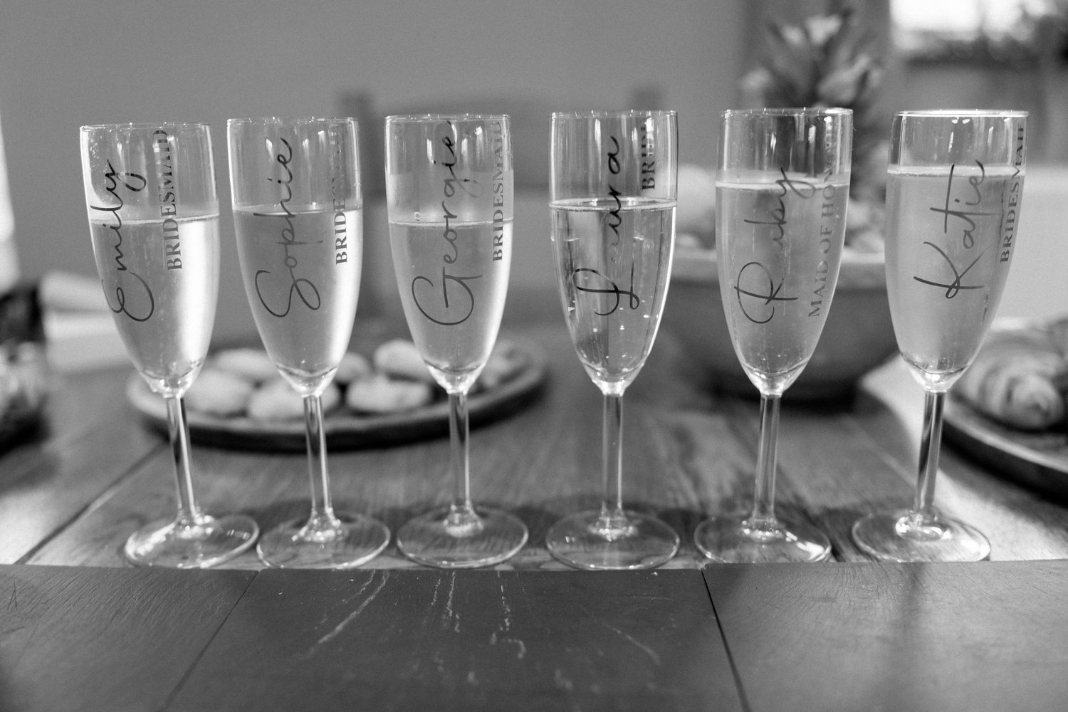 A row of champagne flutes lined up on a dark surface in black and white.