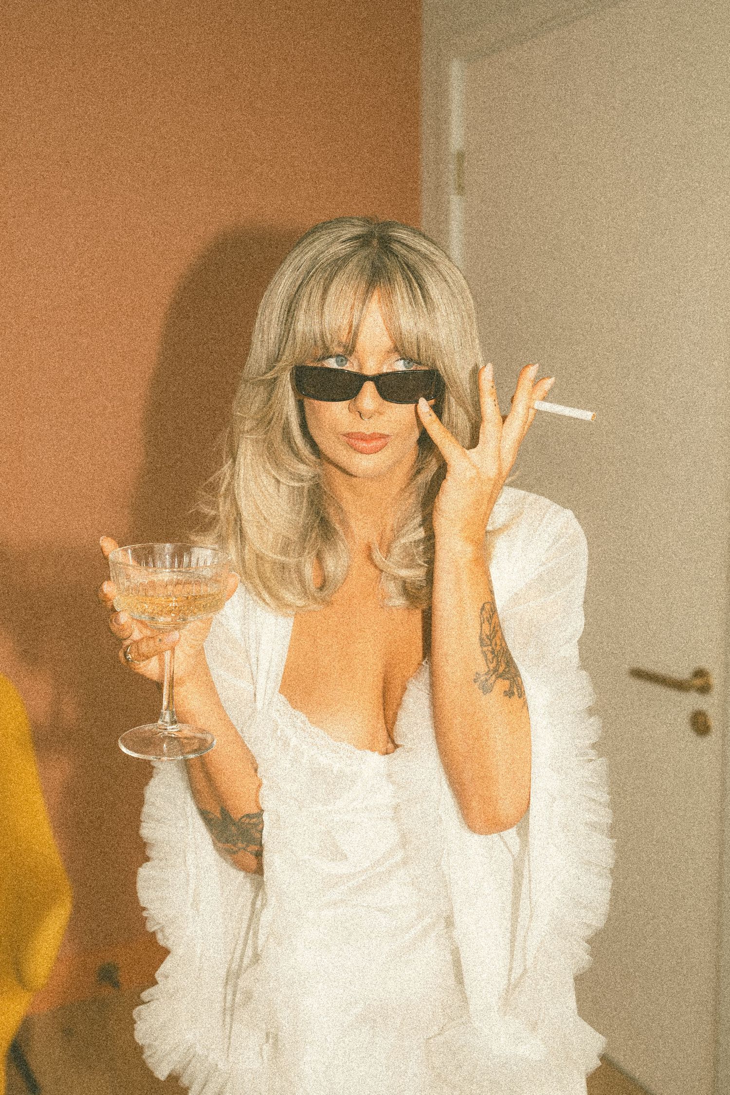 Retro-style photos with sunglasses and white outfit against a warm-toned wall.