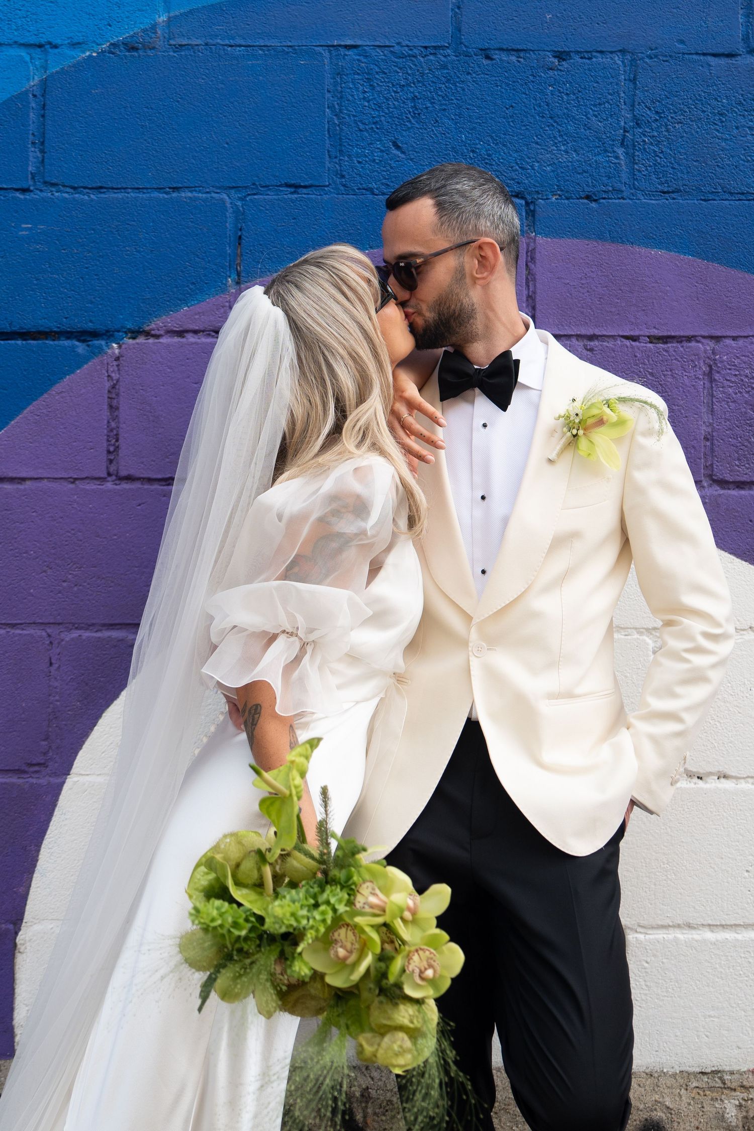 Couple shares intimate moment against vibrant blue and purple wall.