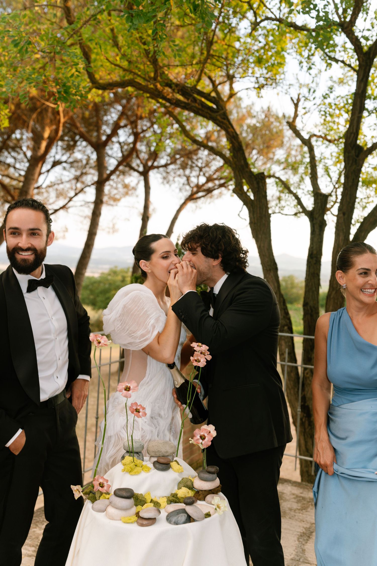Wedding celebration sequence showing guests enjoying refreshments under trees at sunset.