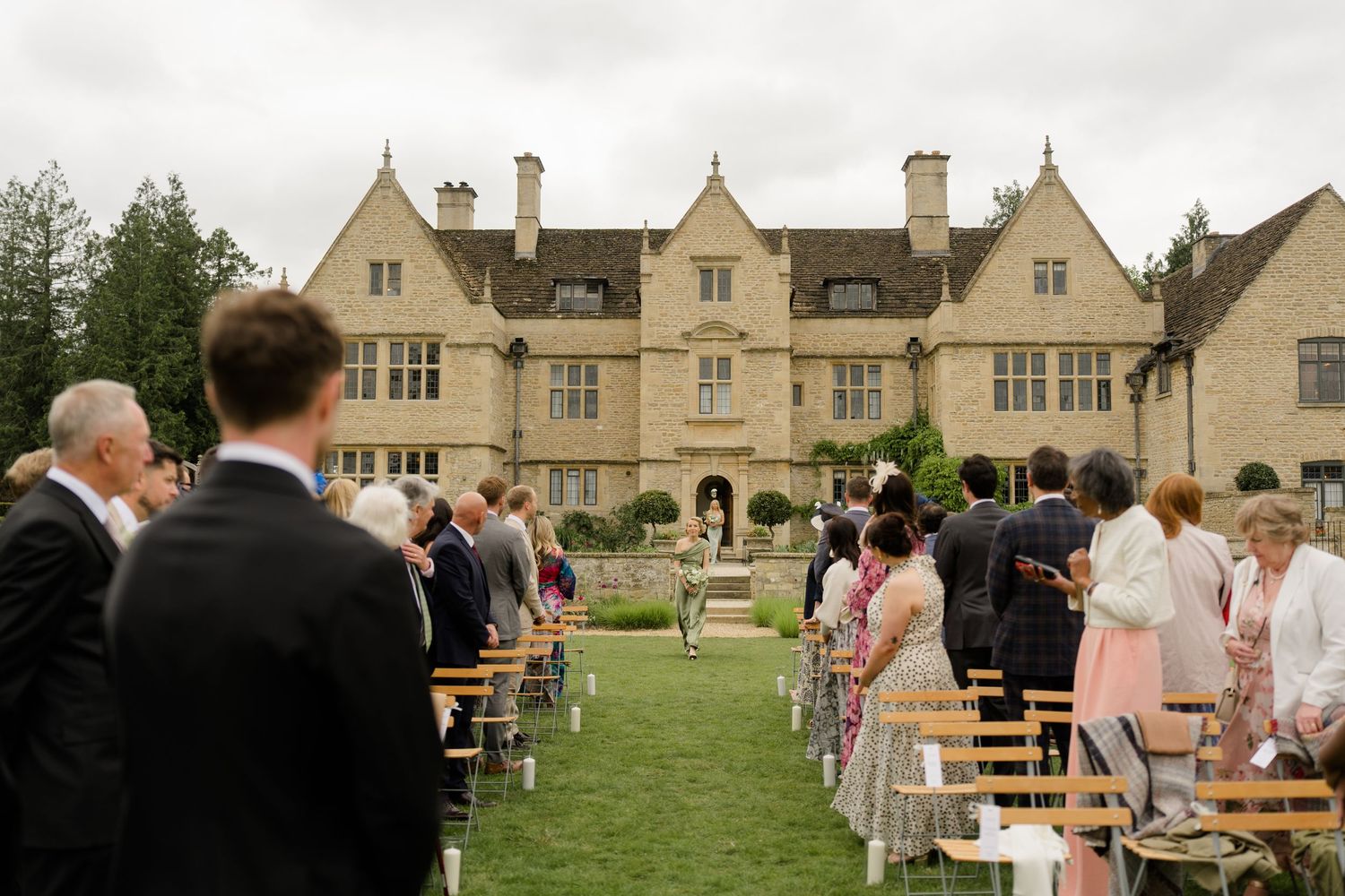 Outdoor wedding ceremony on manicured lawn in front of a grand Cotswolds stone manor house.
