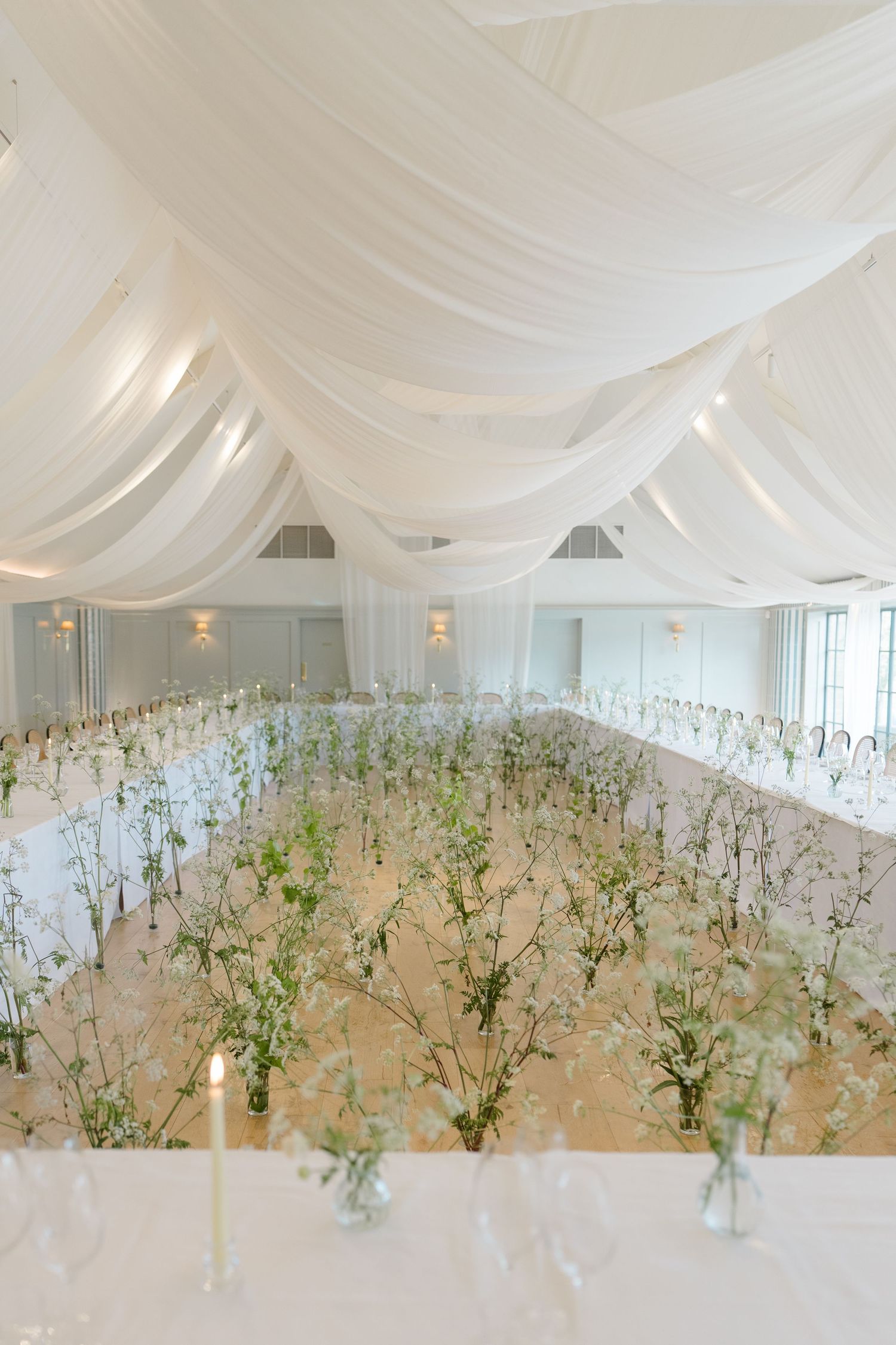 Elegant wedding reception hall with white draped ceiling, long tables adorned with delicate floral centerpieces.