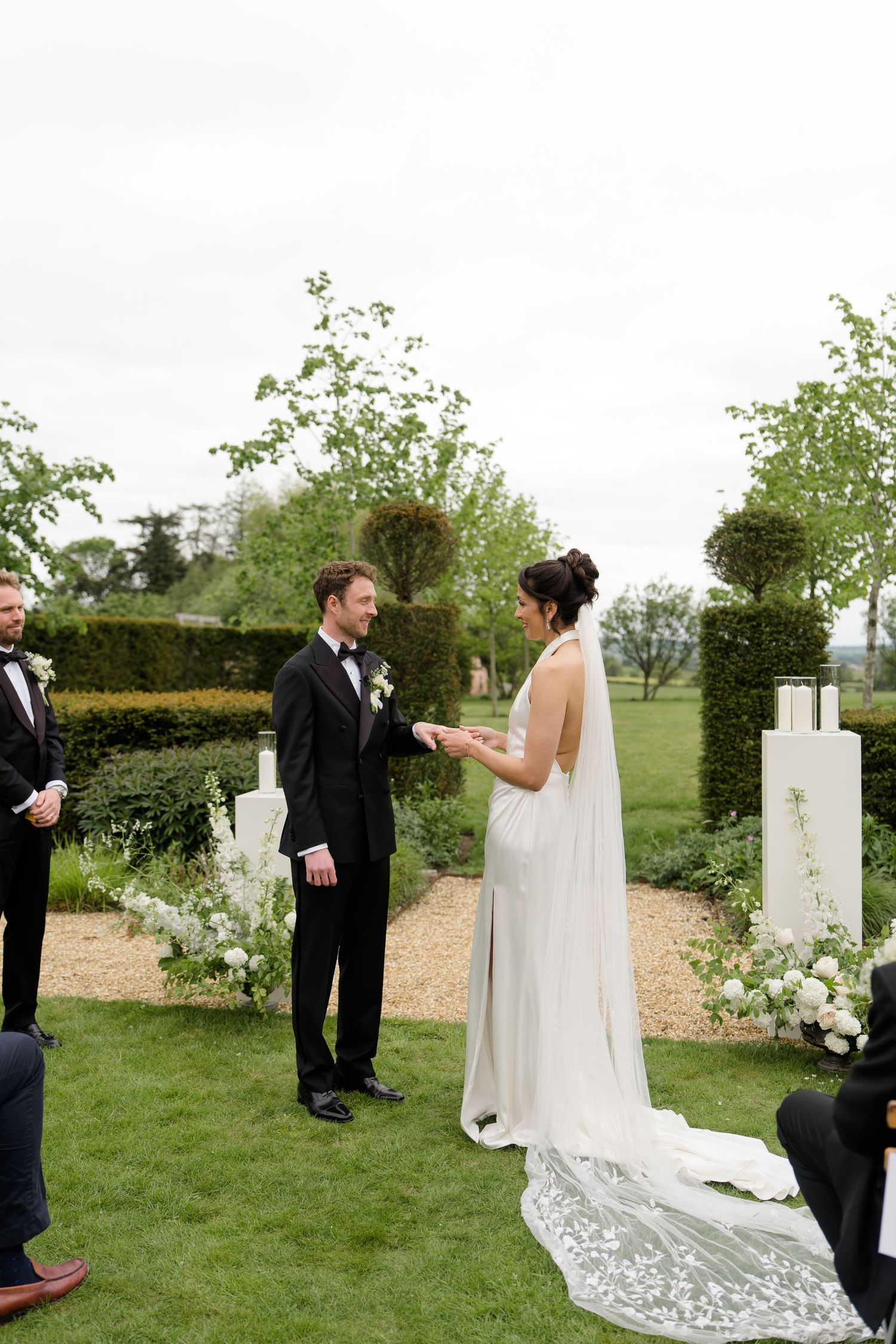 Bride and groom exchanging vows at outdoor garden wedding ceremony with white floral arrangements.