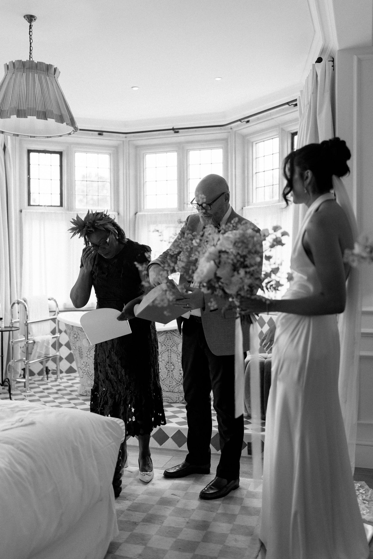 Bride receiving bridal bouquet from guests in elegant bay window bedroom before wedding.