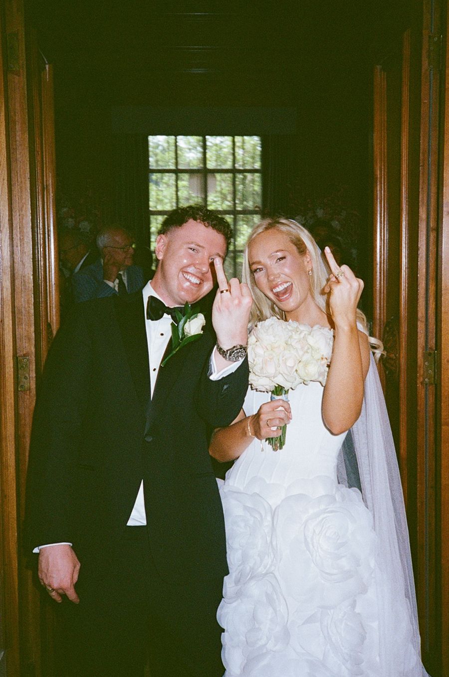 Joyful bride and groom celebrating their wedding day, flashing rock signs, bride holding white bouquet in elegant venue.