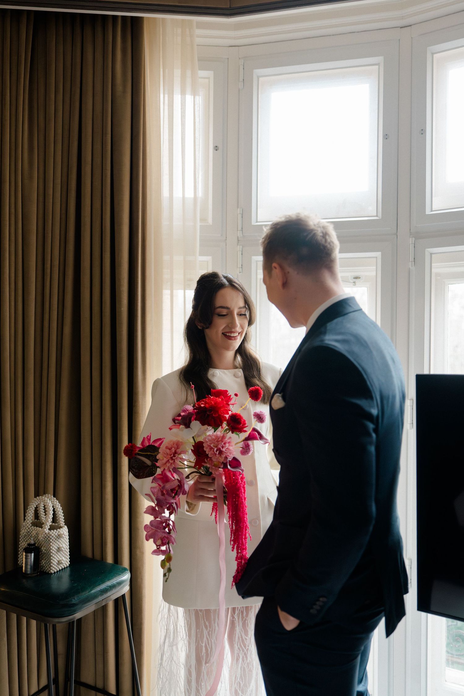 Groom presenting bride with vibrant red and pink floral bouquet in hotel room.