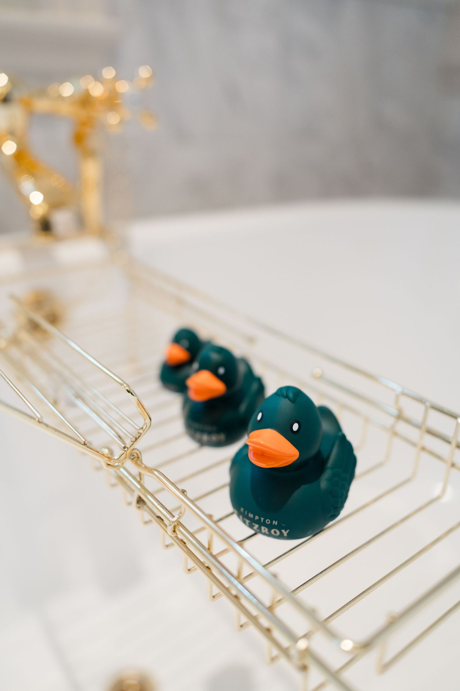 Two dark green rubber ducks with orange beaks on a gold bath caddy tray.