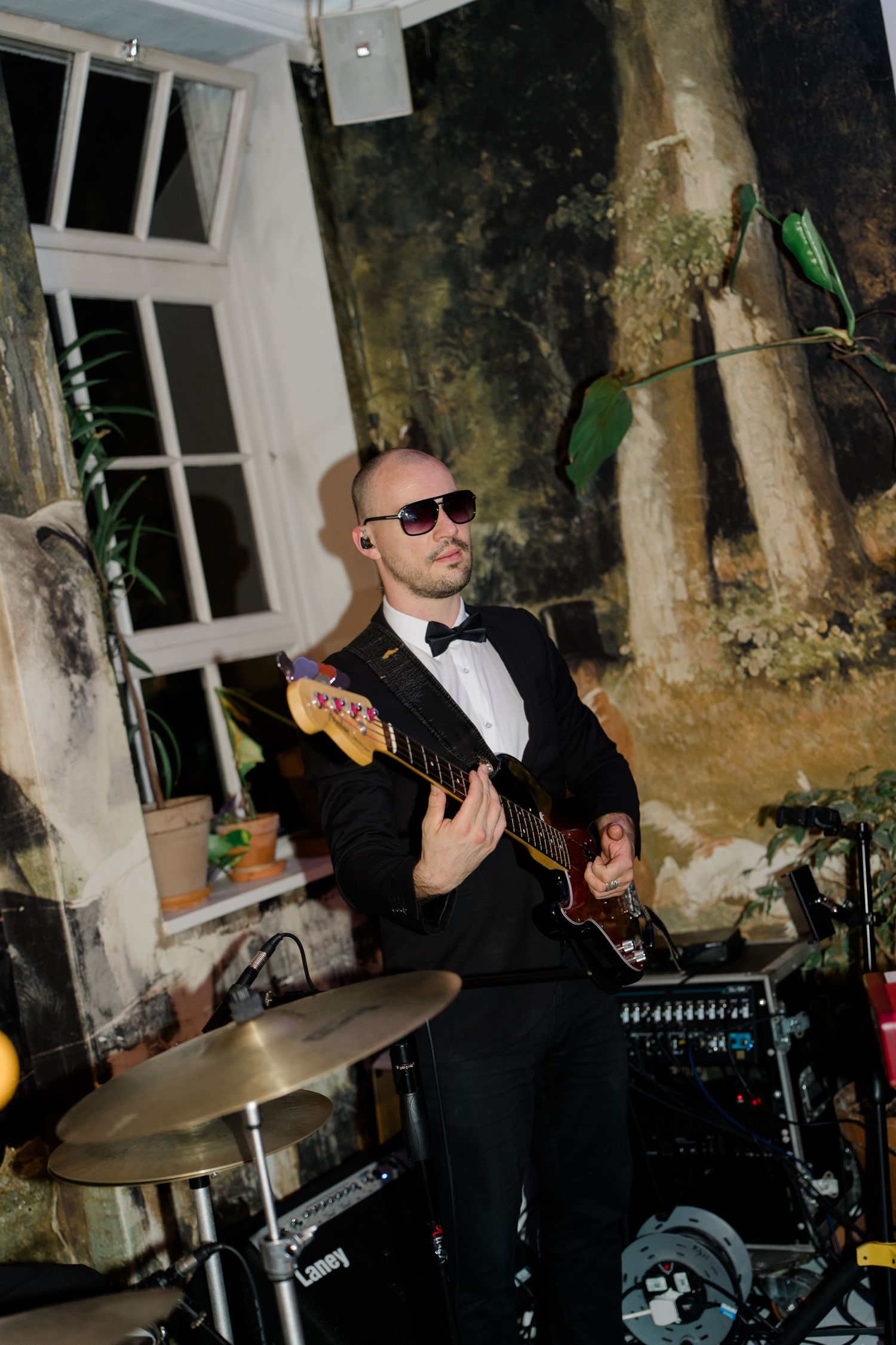 Musician in a tuxedo playing electric guitar at a wedding reception with a painted backdrop.