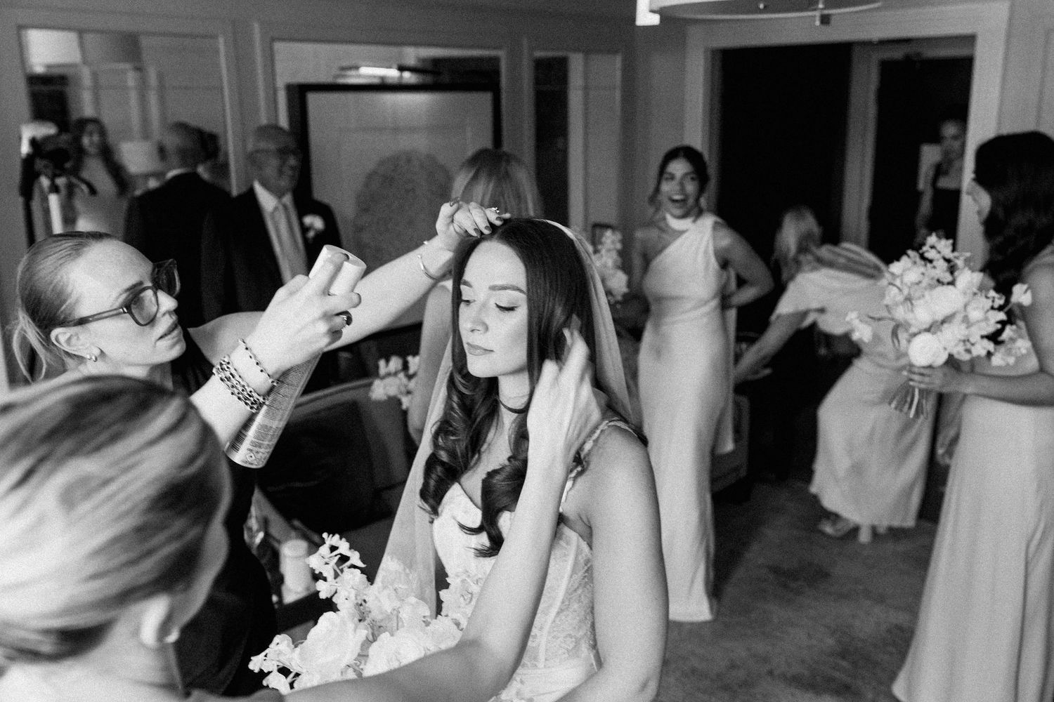 Bridesmaids helping bride with veil before wedding ceremony in black and white photo.