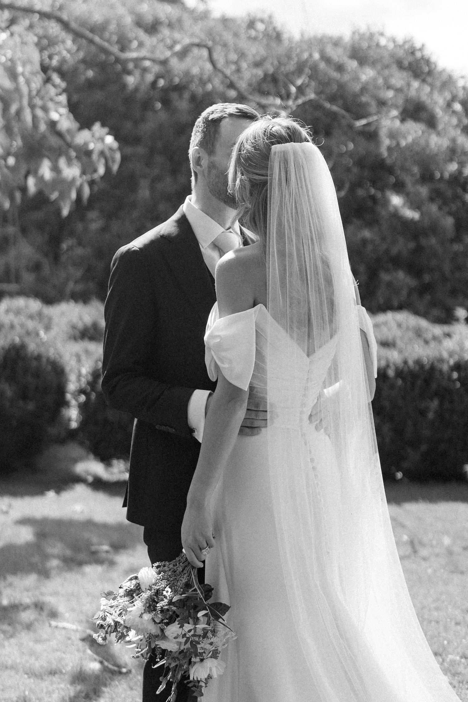 Black and white wedding portrait showing flowing veil and bouquet details.