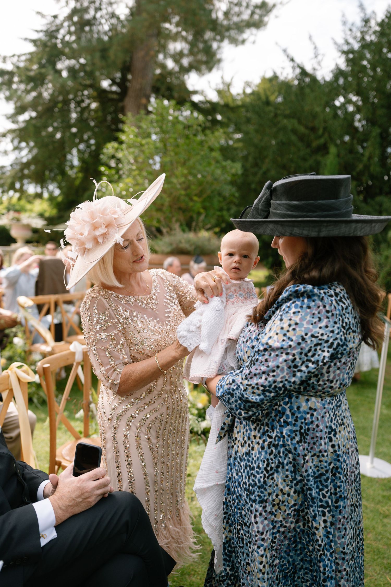 Wedding guests in formal attire sharing an emotional moment during an outdoor ceremony.