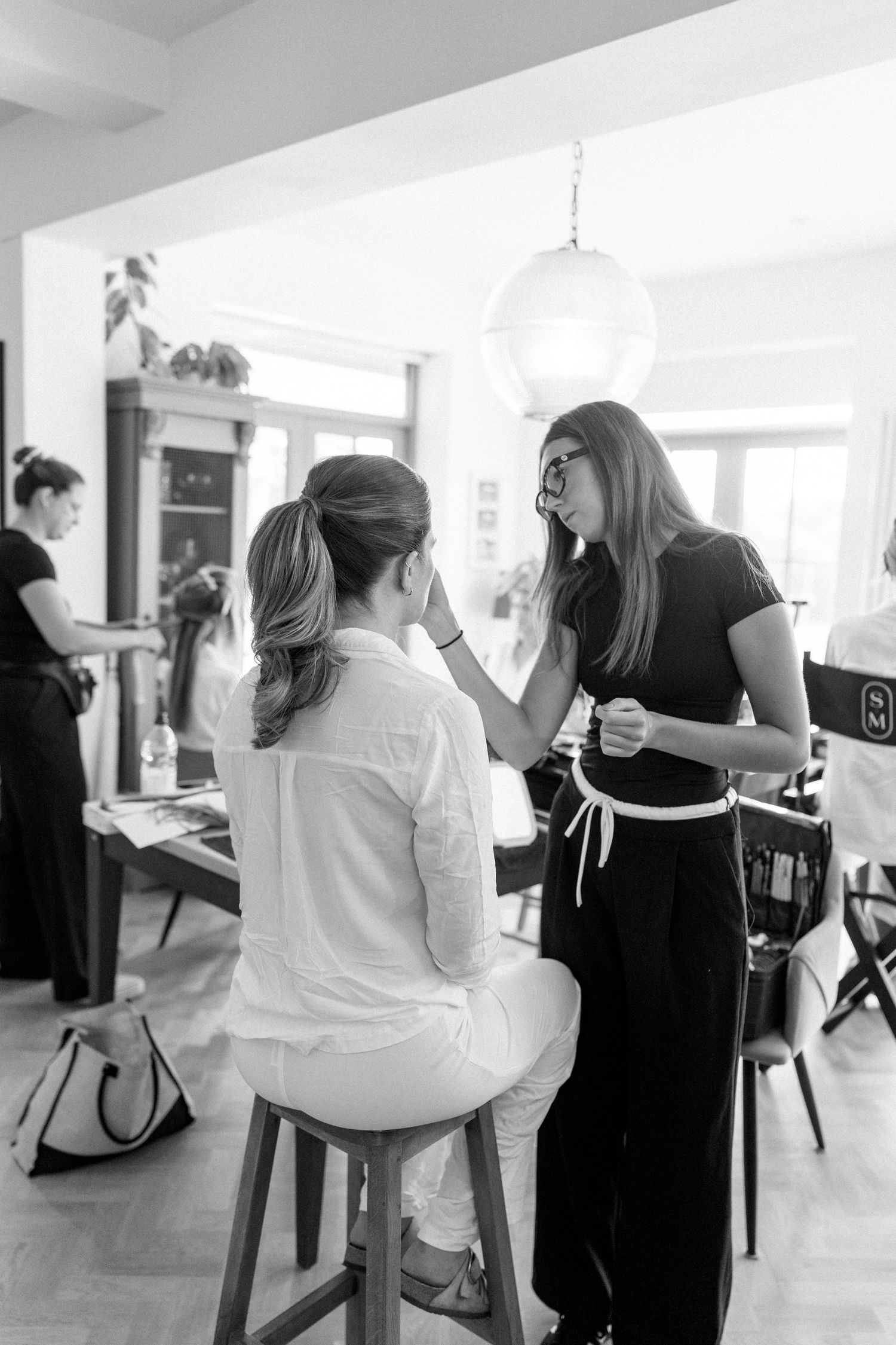 Black and white image of beauty professionals preparing clients in a bright studio space.