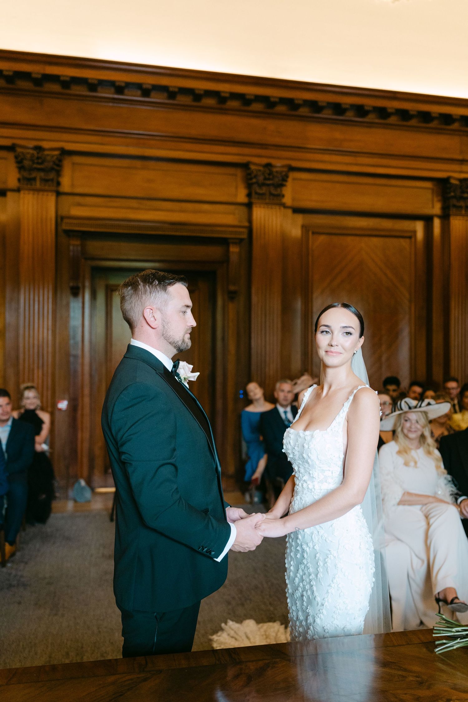 A couple shares their first dance in an elegant wood-paneled ballroom.