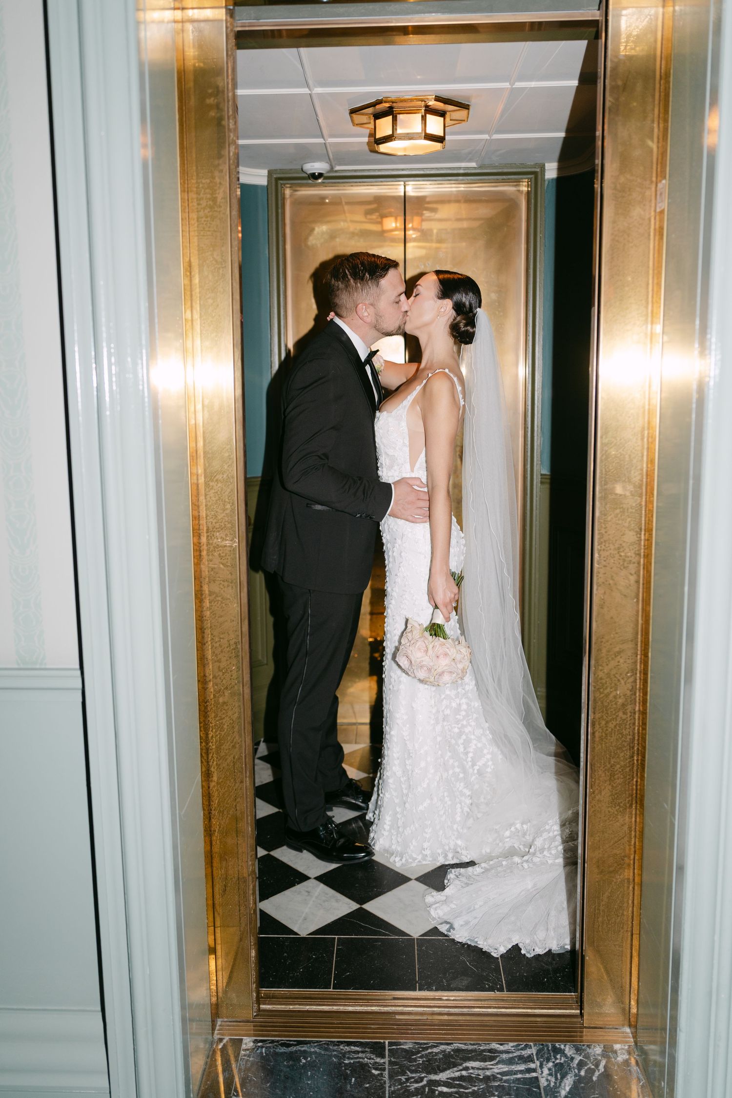 A romantic wedding couple sharing a kiss in an elegant gold-trimmed elevator.