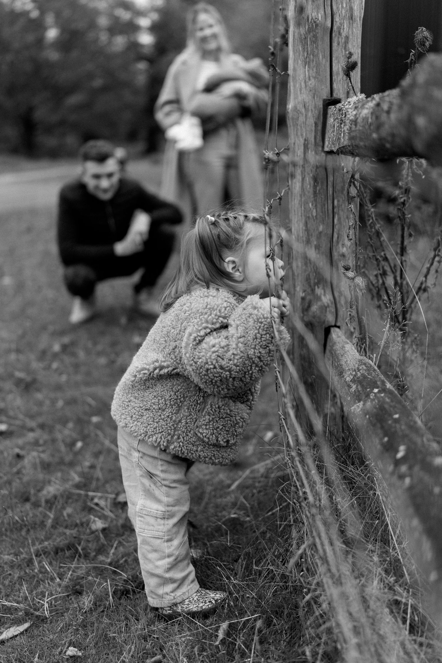 Black and white photograph of a small child exploring near a wooden fence.