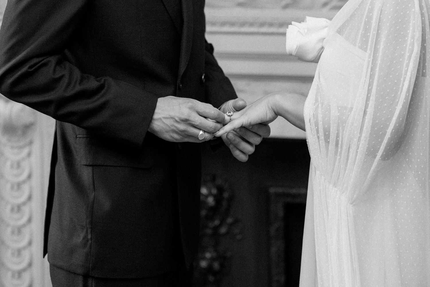 Wedding ceremony in progress in an elegant room with white walls and decorative molding.