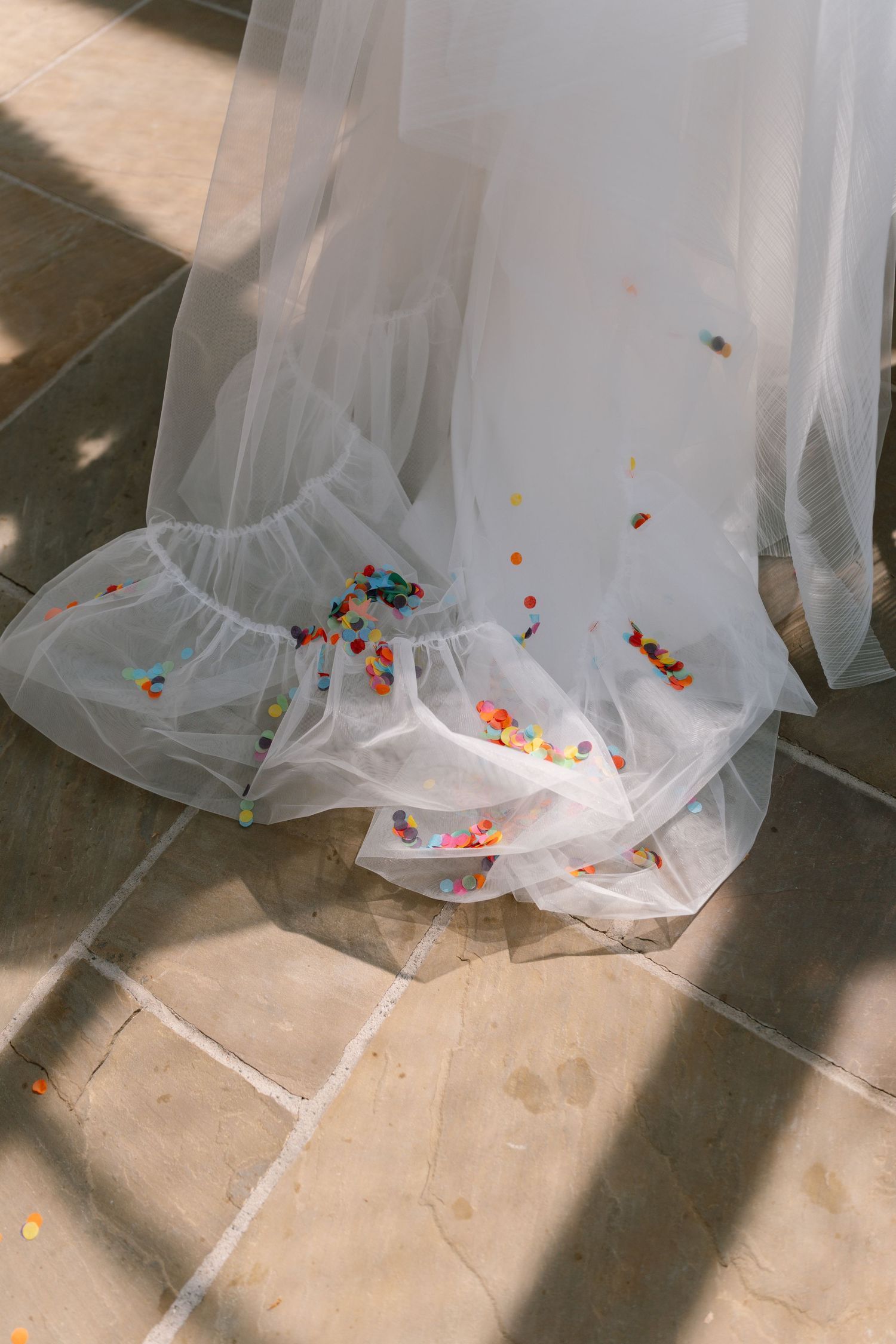 Colorful confetti scattered beneath the flowing layers of a white wedding dress.