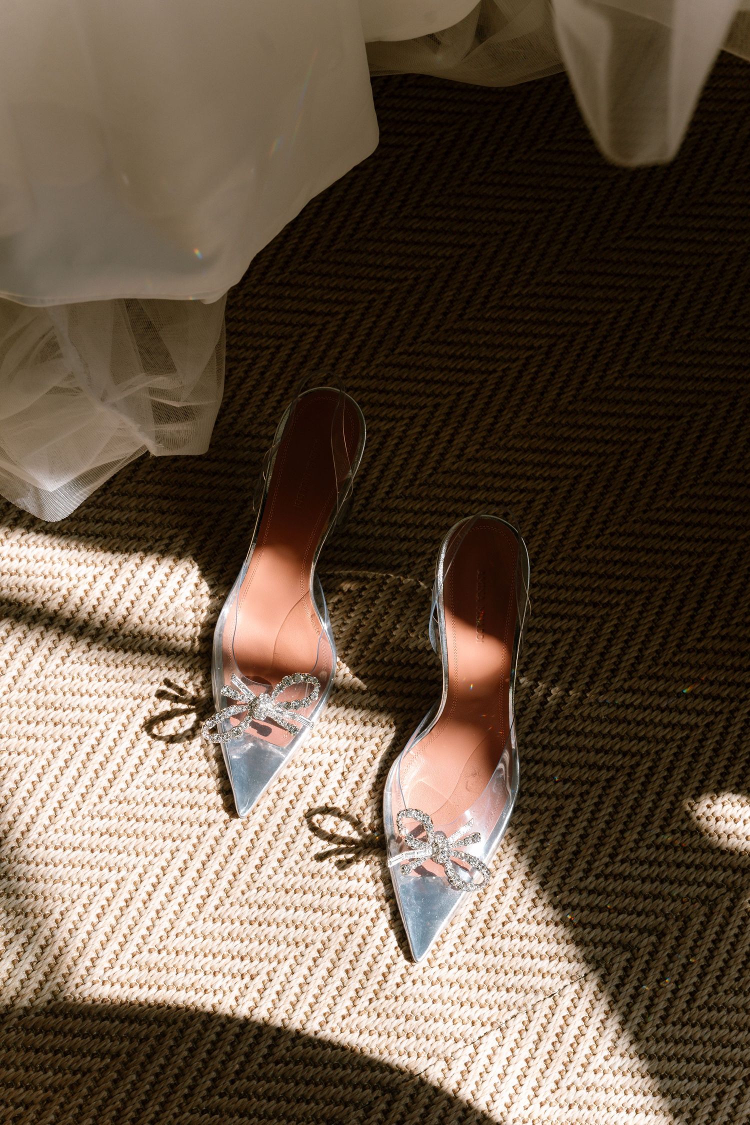 Blue bridal shoes with embellishments catching sunlight on dark carpet.